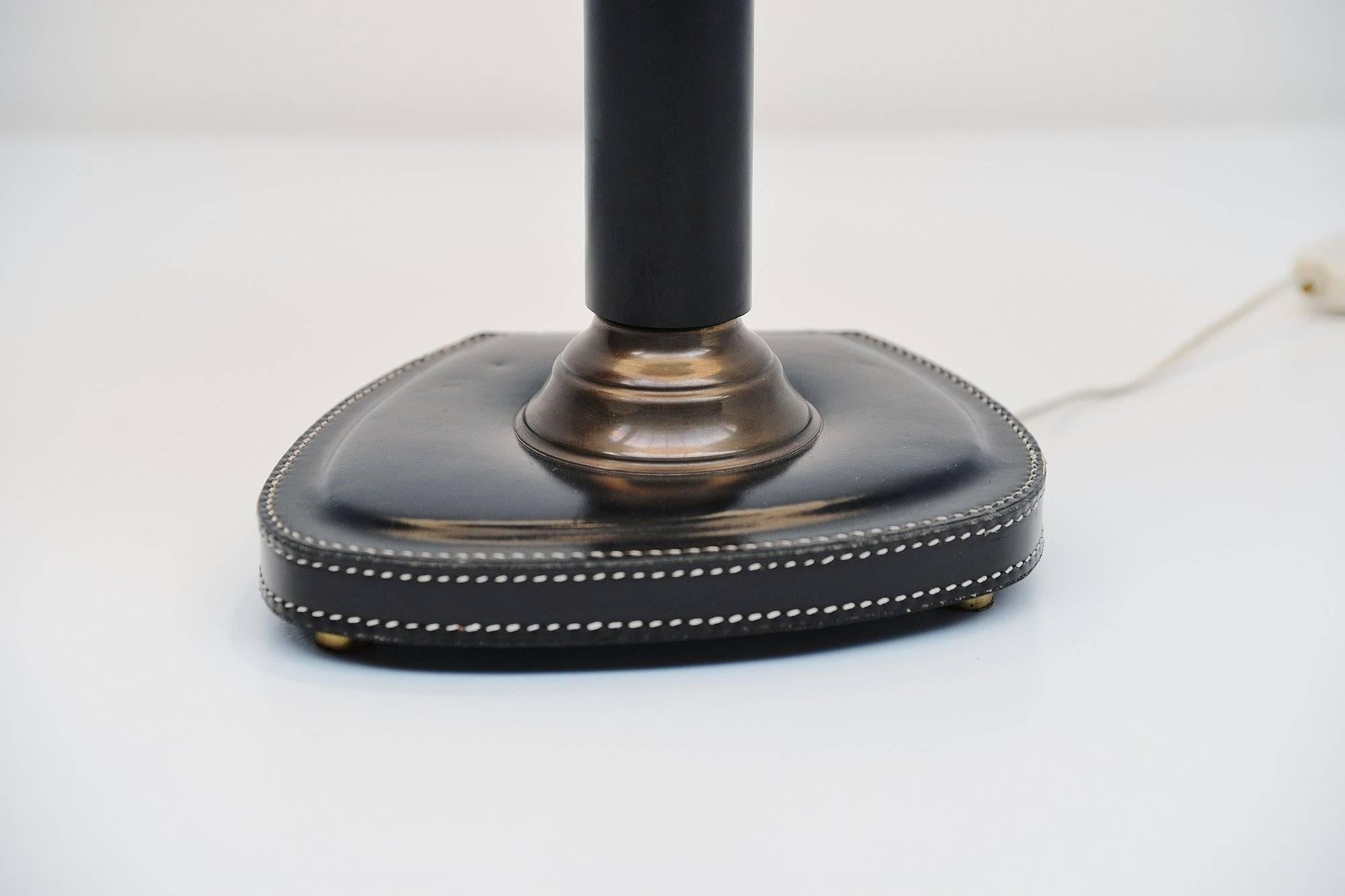Nice and decorative table lamp in the style of Jacques Adnet, France 1960. This table lamp has a black stitched leather foot and brass details. The shade is newly covered with off white fabric. The lamp gives very nice and warm light when lit and is