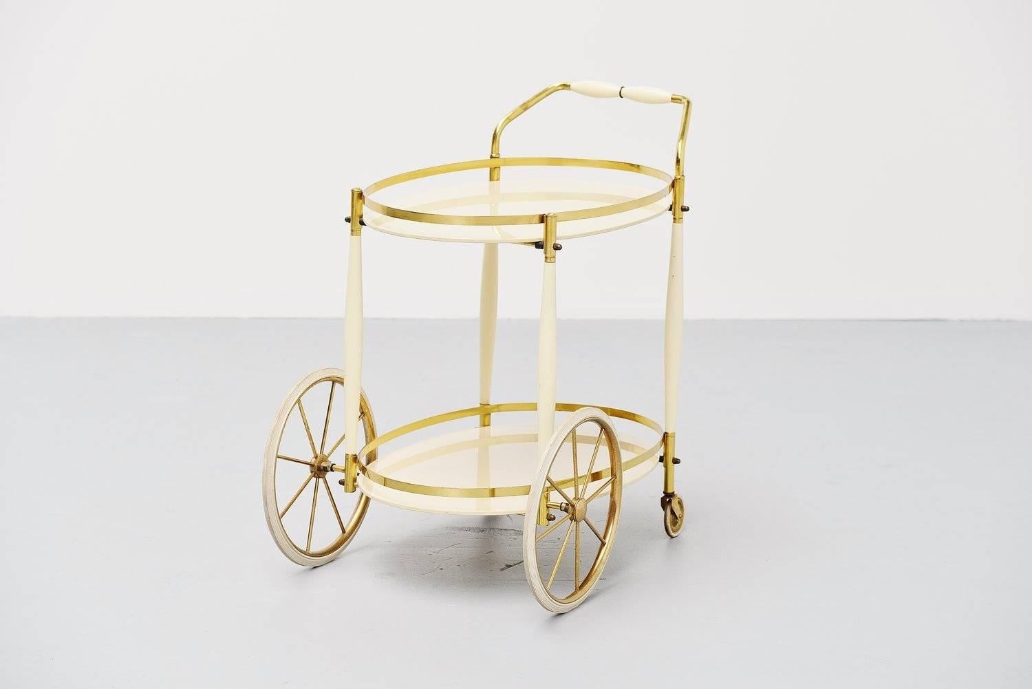 Decorative tea cart made by unknown manufacturer or designer but Italian for sure. Manufacturer circa 1950. This cart is made of brass and has white opaline glass trays, and a white lacquered wooden handle. The wheels are made of rubber and ride