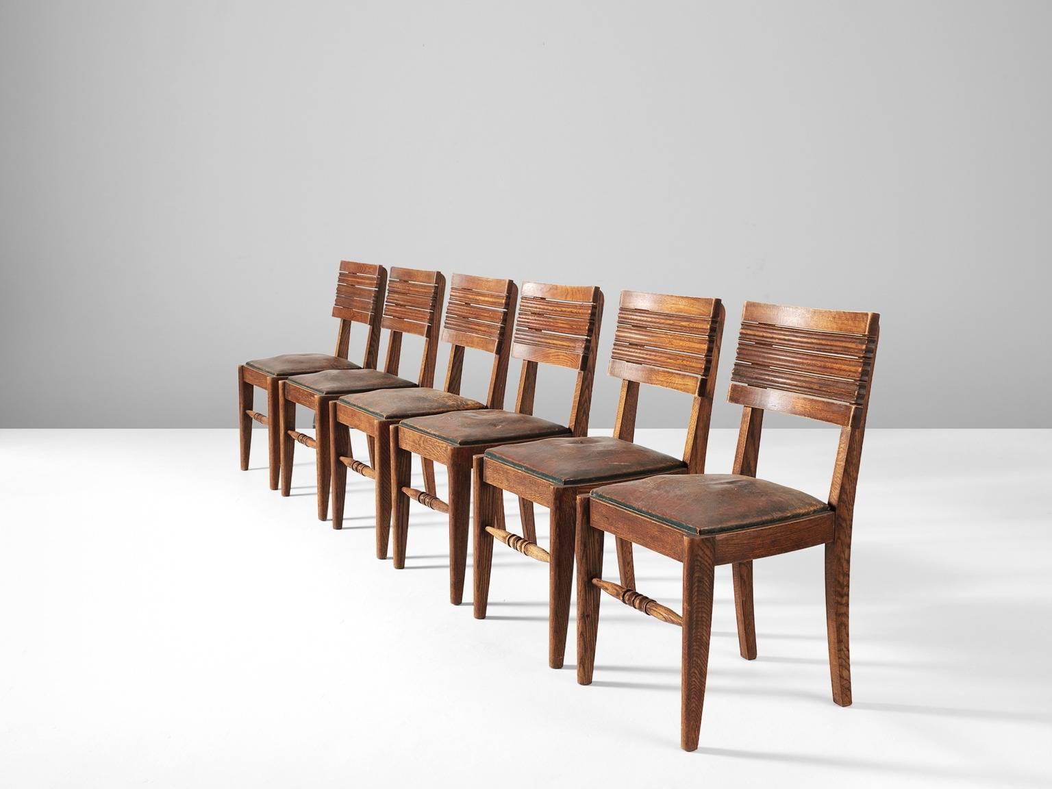 Set of six dining chairs, in oak and leather, by Gaston Poisson, France 1940s.

Dining chairs in solid oak, with beautiful detailed woodcarving and stunning patinated leather. The back of the chair consist of five slightly curved slats: top and