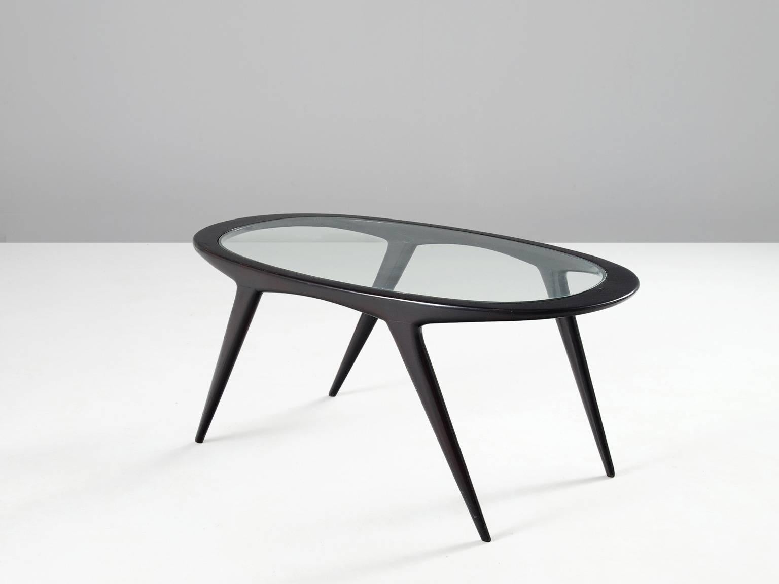 Cocktail table, in glass and wood, Italy, 1950s. 

Oval shaped coffee table in glass and ebonized wood. The black lacquered frame shows four nice tapered legs which fluently go over into the oval shaped top. The clear glass makes a nice contrast