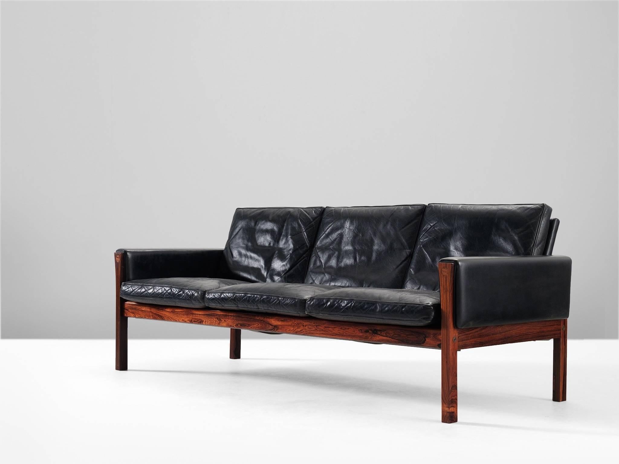 Three seat sofa, in black leather and rosewood, by Hans J. Wegner, Denmark, 1960s. 

Excellent designed sofa by Hans Wegner. The straight lines of this design show an amazing elegance. The rosewood frame is well proportioned. The way the legs