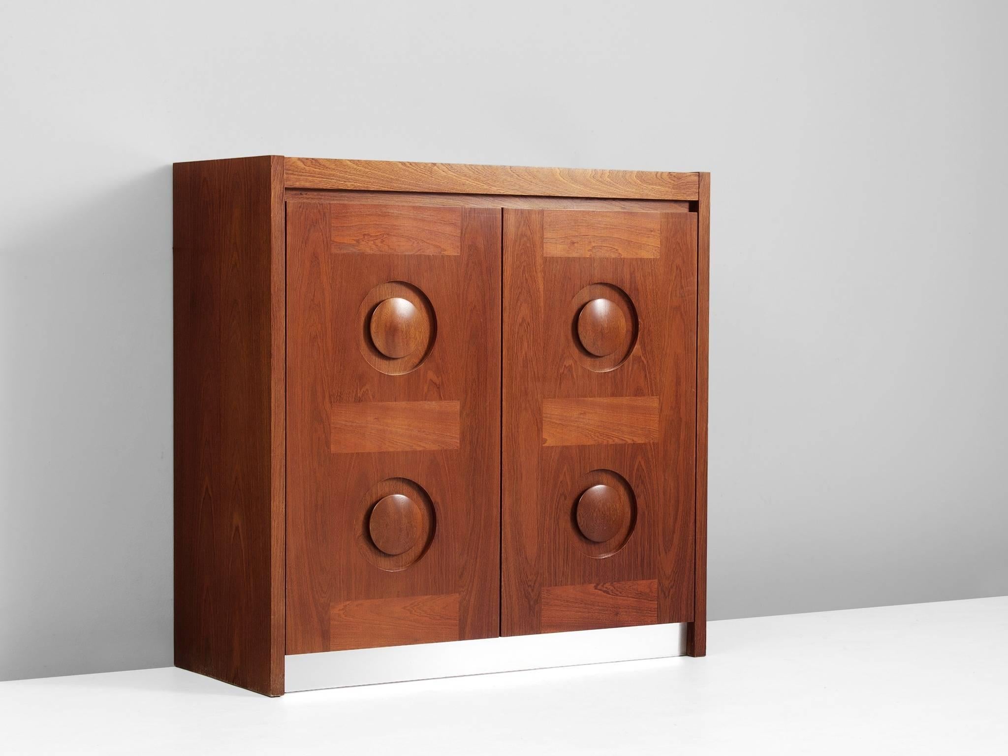 Brutalist credenza, in mahogany and aluminum, European, 1970s.

Sturdy illuminated bar cabinet in mahogany with graphical designed door panels. Two-door panels, each with a three-dimensional pattern of circles and horizontal lines, which gives the