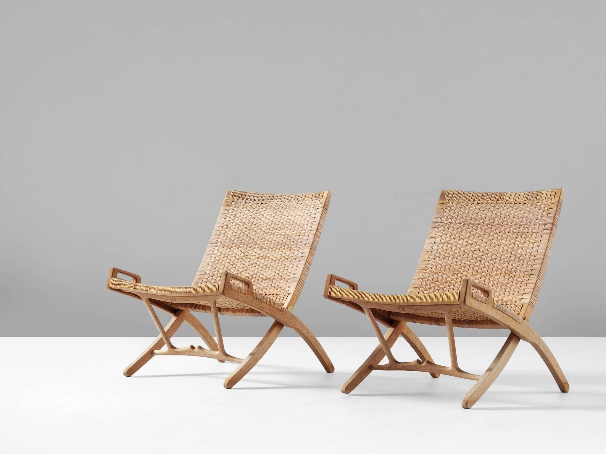 Pair of folding chairs model JH512, in oak and cane, by Hans J. Wegner for Johannes Hansen, Denmark, 1949. 

These chairs were designed by Hans Wegner for the small post-war home. To save space they can be fold together and hung on the wall. At
