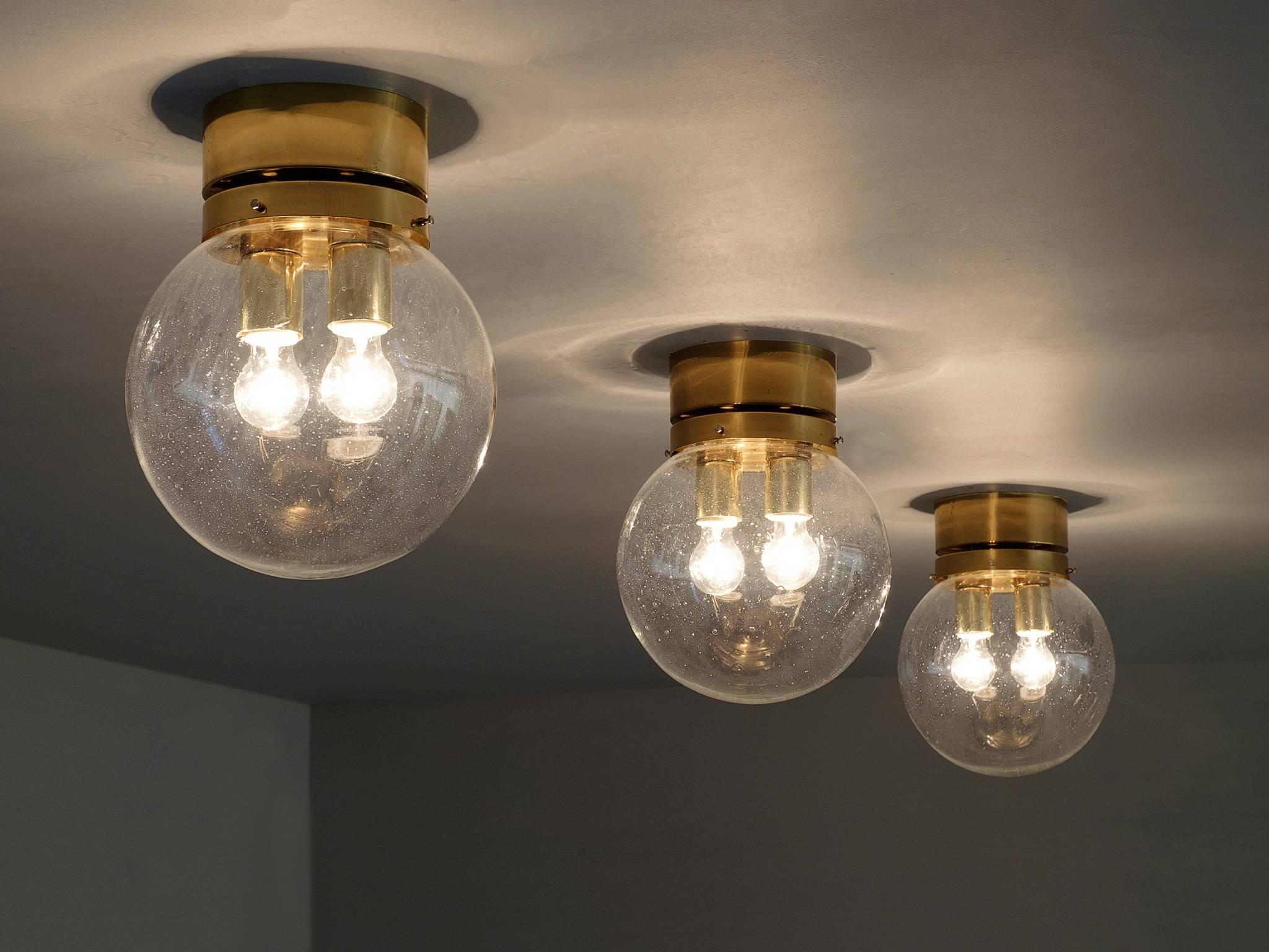 Set of 5 flush mount lights, in glass and brass, Europe, 1970s.

Set of modern and minimalistic ceiling lights in brass and glass. Each light consist of a round brass fixture and a raindrop glass sphere. Inside the sphere are two light-points. The