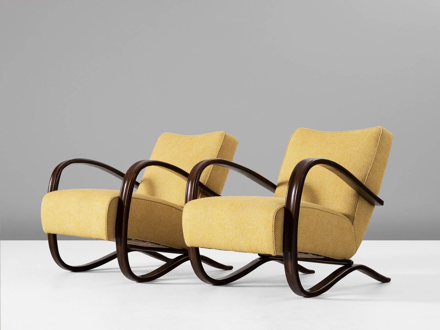 Pair of armchairs, in beech and yellow fabric, by Jindrich Halabala, Czech Republic, 1930s.

These chairs have a very dynamic appearance, due the curved base that ends fluently in the armrests. The dark brown stained wood nicely contrast to the