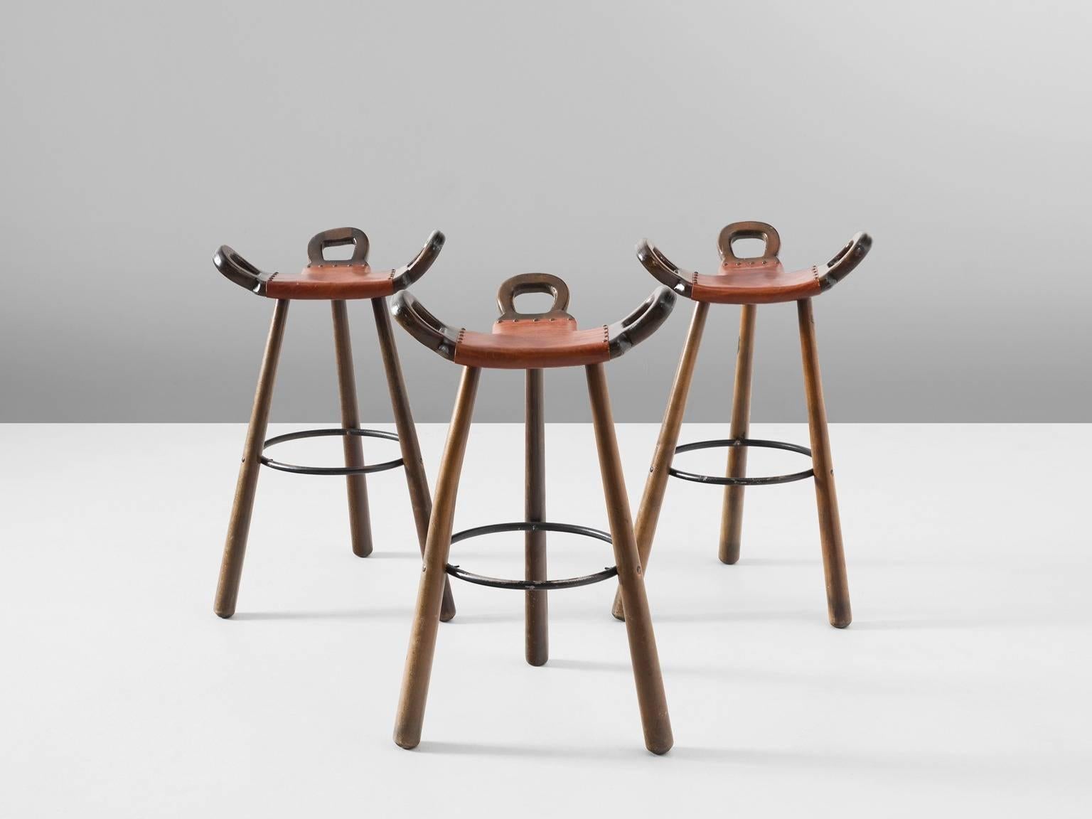 Set of three 'Brutalist' or 'Marbella' bar stools, in stained beech, leather and metal, Spain, 1970s. 

Set of three Brutalist bar stools in dark-brown stained beech. The eye-catching part is the seating. A curved T-shape with three handles. The