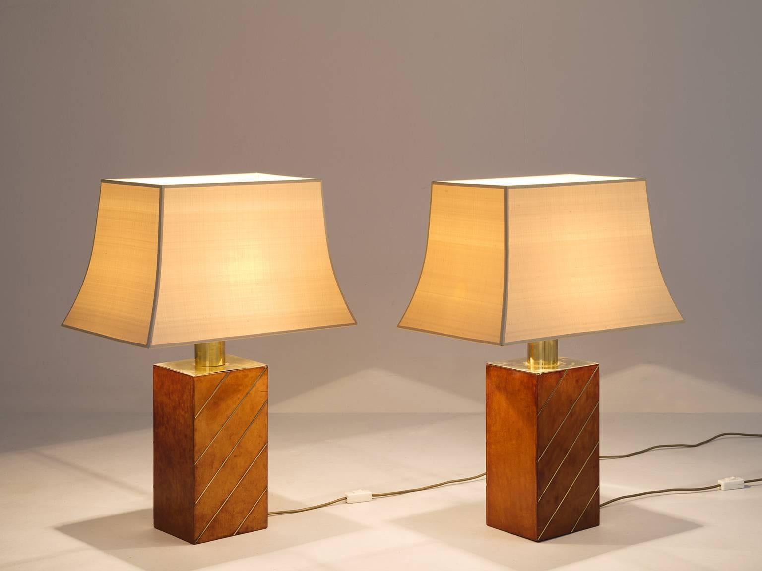 Pair of table lamps, in leather brass and fabric, Europe, 1970s. 

Nice pair of table lamps with beautiful leather wrapped base. The cognac leather beautifully combines with the brass colored fixture. The off-white fabric shade is a nice addition