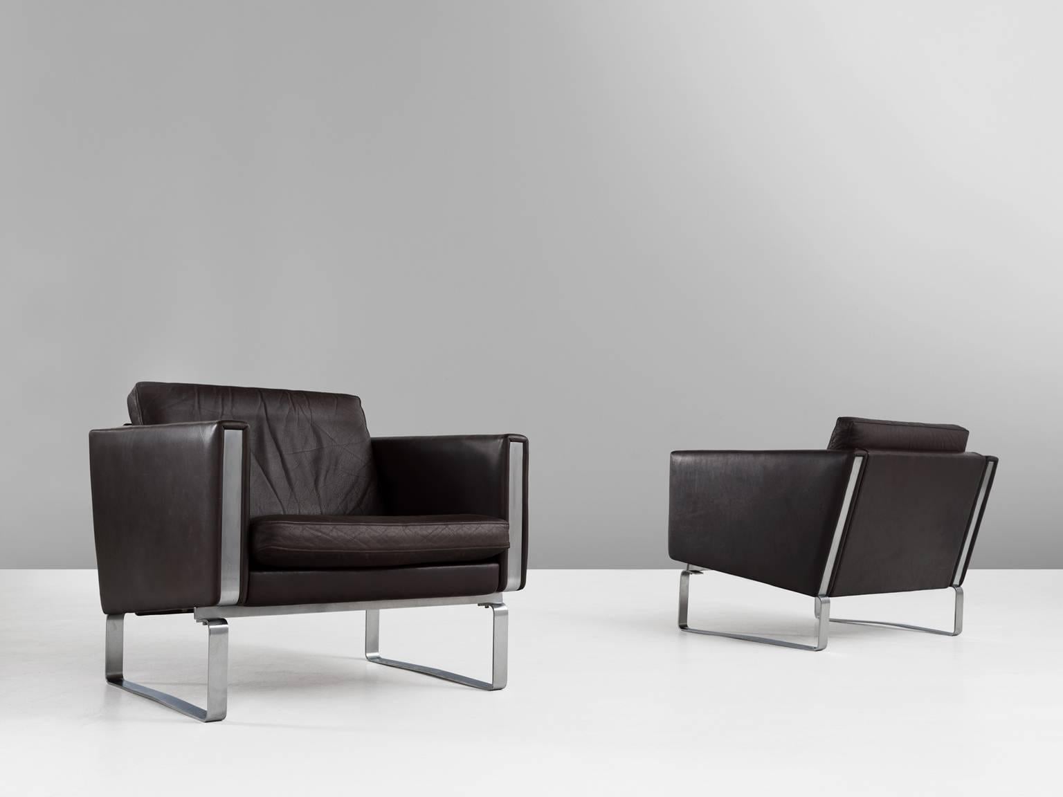 Set of two lounge chairs, in leather and metal, by Hans J. Wegner for Johannes Hansen, Denmark 1970s.

Pair of modern armchairs in dark brown leather by Hans Wegner. Due the materials, the leather and steel, these chairs get their characteristic