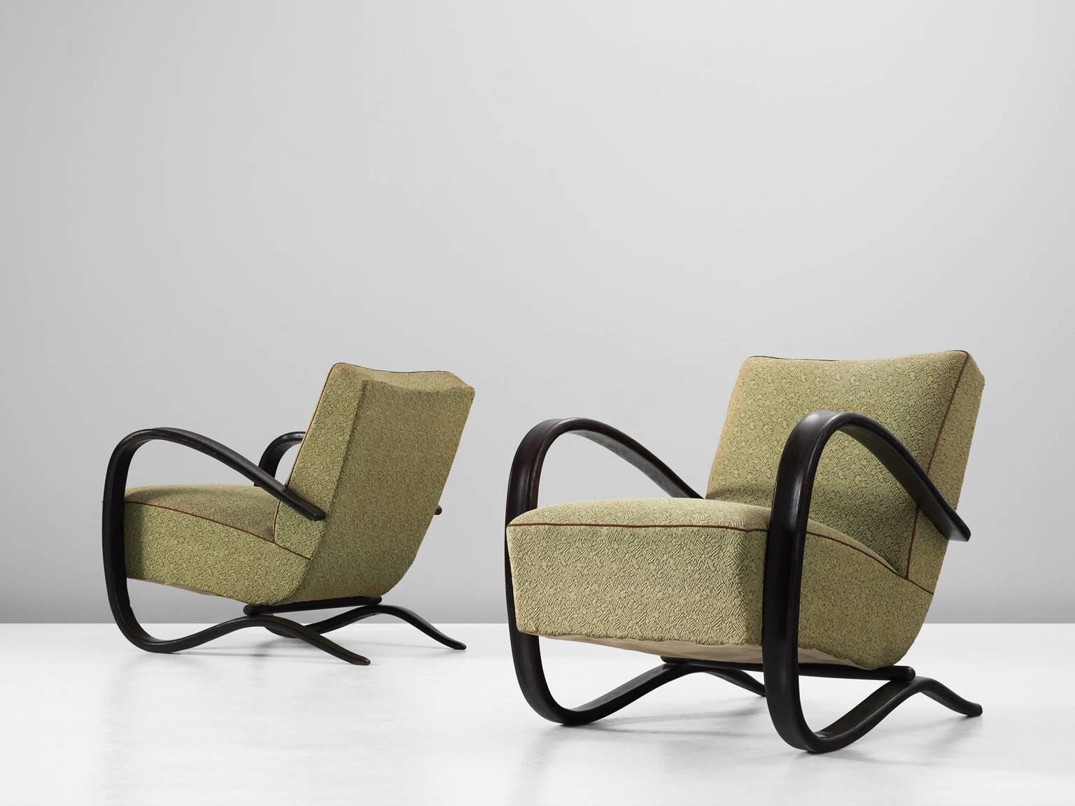 Pair of armchairs, in beech and fabric, by Jindrich Halabala, Czech Republic, 1930s. 

These chairs have a very dynamic appearance, due the curved base that ends fluently in the armrests. The dark brown stained wood nicely contrast to the green