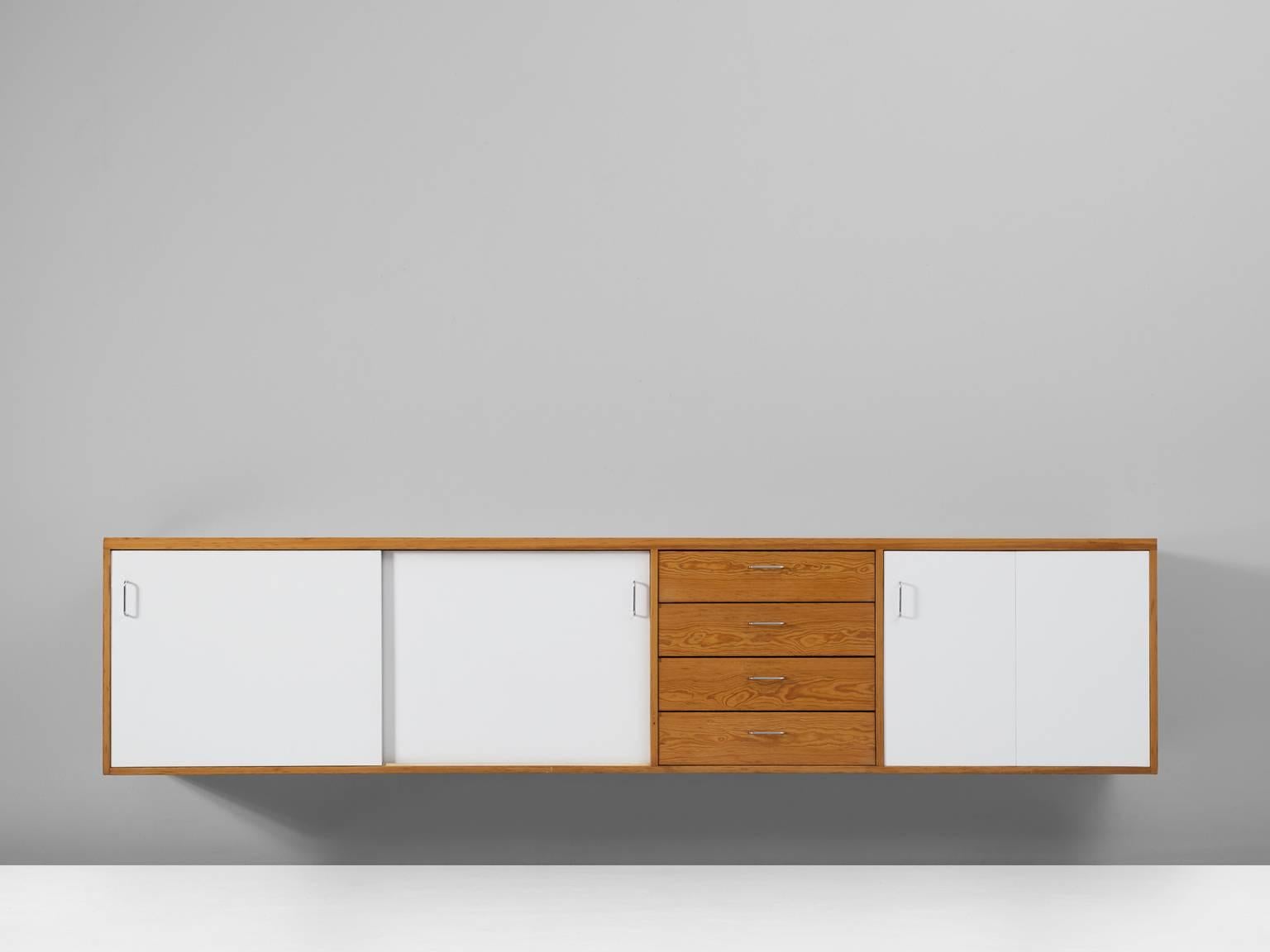 Cabinet, in pine, plywood and metal, Europe, 1970s.

Wall-mounted cabinet in natural pine and white coated plywood. Three white doors on the front are interrupted by a section of four drawers in blond wood. The doors on the left are sliding door,