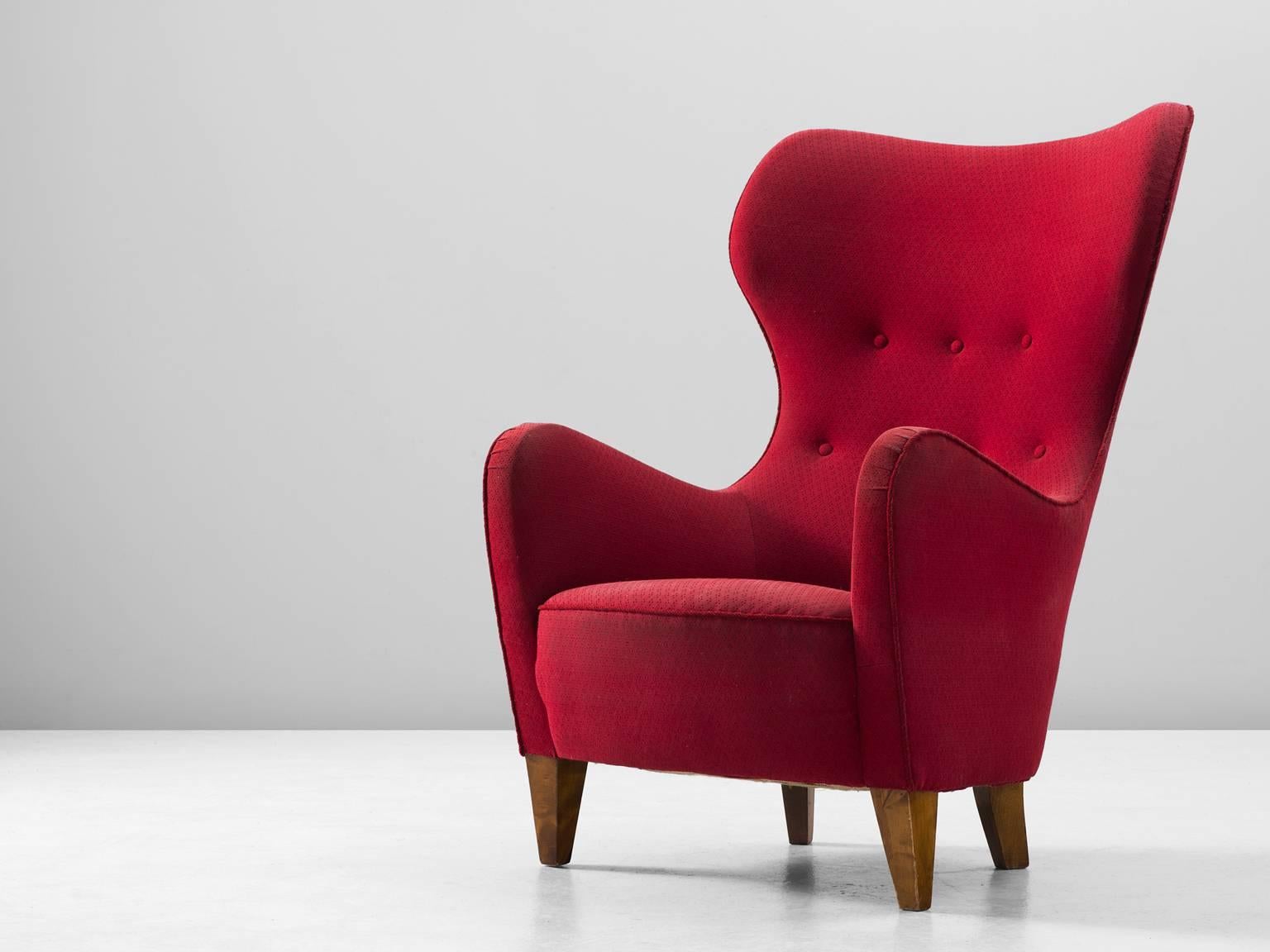 Wingback chair, in wood and fabric, Scandinavia, 1950s.

High back chair in red fabric upholstery. This chair shows the characteristics of the Scandinavian Modern style and great resemblance to the early lounge chairs of Fritz Hansen and Rud