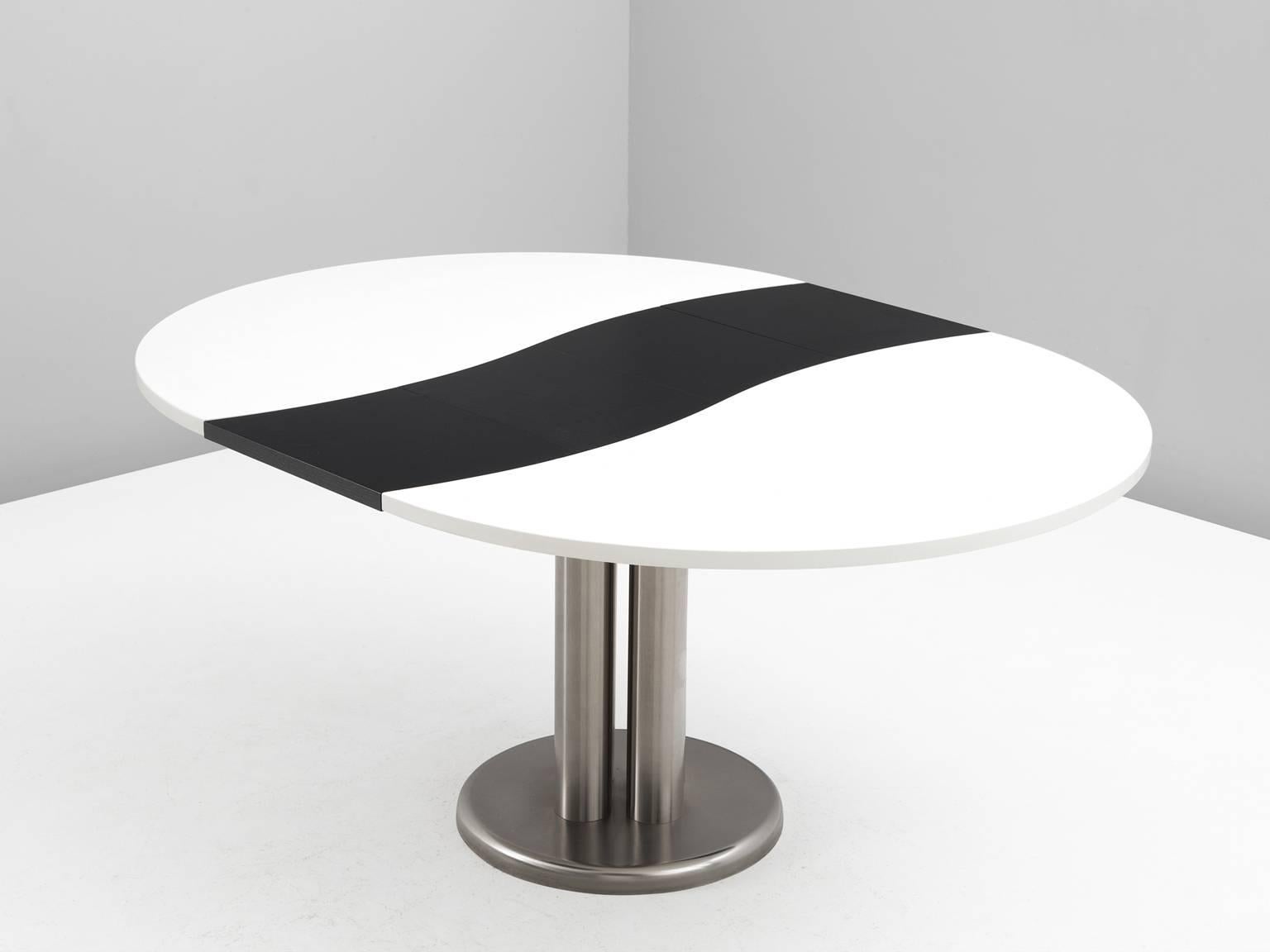 Extendable table, in stainless steel and wood, by Studio D'Urbino Lomazzi, Italy, 1969.

Oval dining table, with monochrome colored top. The top consist of a large white oval shape with a black wave in the center. The leg consist of four columns