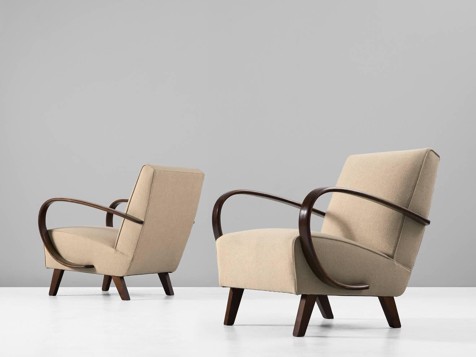 Pair of armchairs, in beech and fabric, by Jindrich Halabala, Czech Republic 1930s.

 Dynamic armchairs with beautiful fluent armrests. The four tapered legs provide a nice open look. The dark brown stained wood nicely blends with the beige woolen