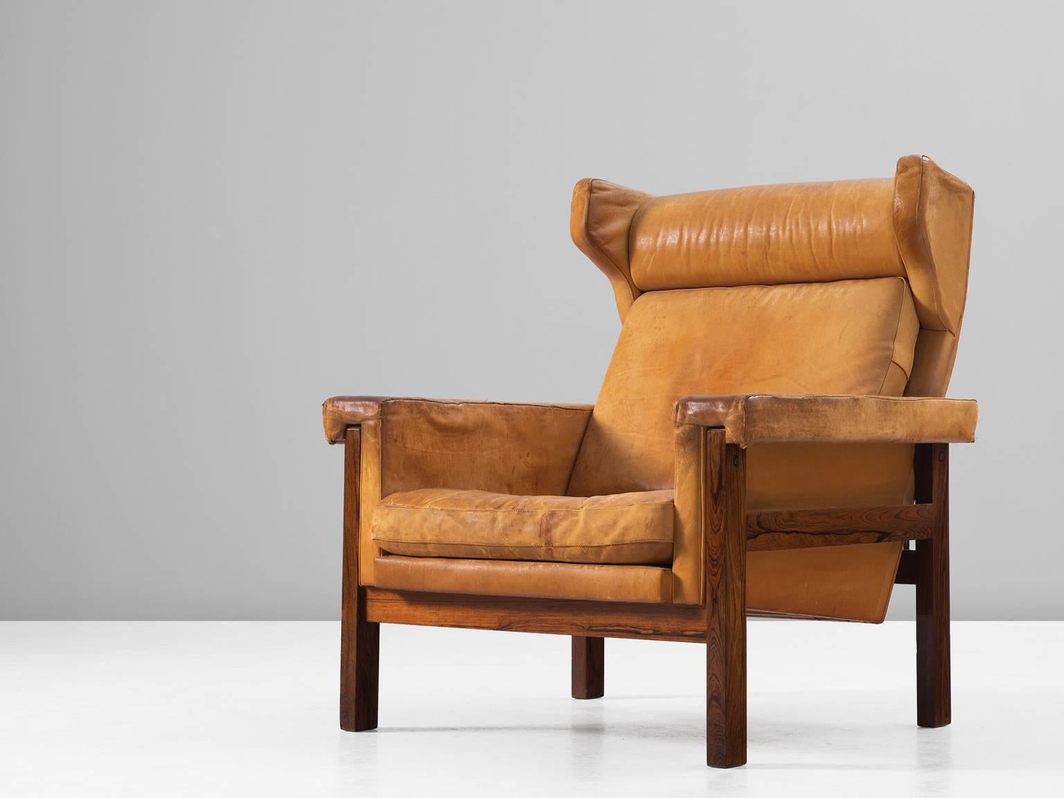 Wingback chair, in rosewood and leather, Denmark, 1960s.

Interesting wingback chair with solid rosewood frame and cognac leather upholstery. This chair shows interesting lines. It shows the classical elements of a lounge chair by Frits Henningsen