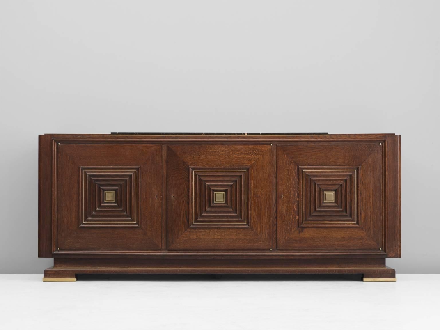 Credenza, in oak marble and brass, France, 1930s. 

Large Art Deco sideboard in the style of Maxime Old. This heavy, almost Brutalist, credenza seems to float on its elegant base with stunning brass detailing. The credenza is equipped with three