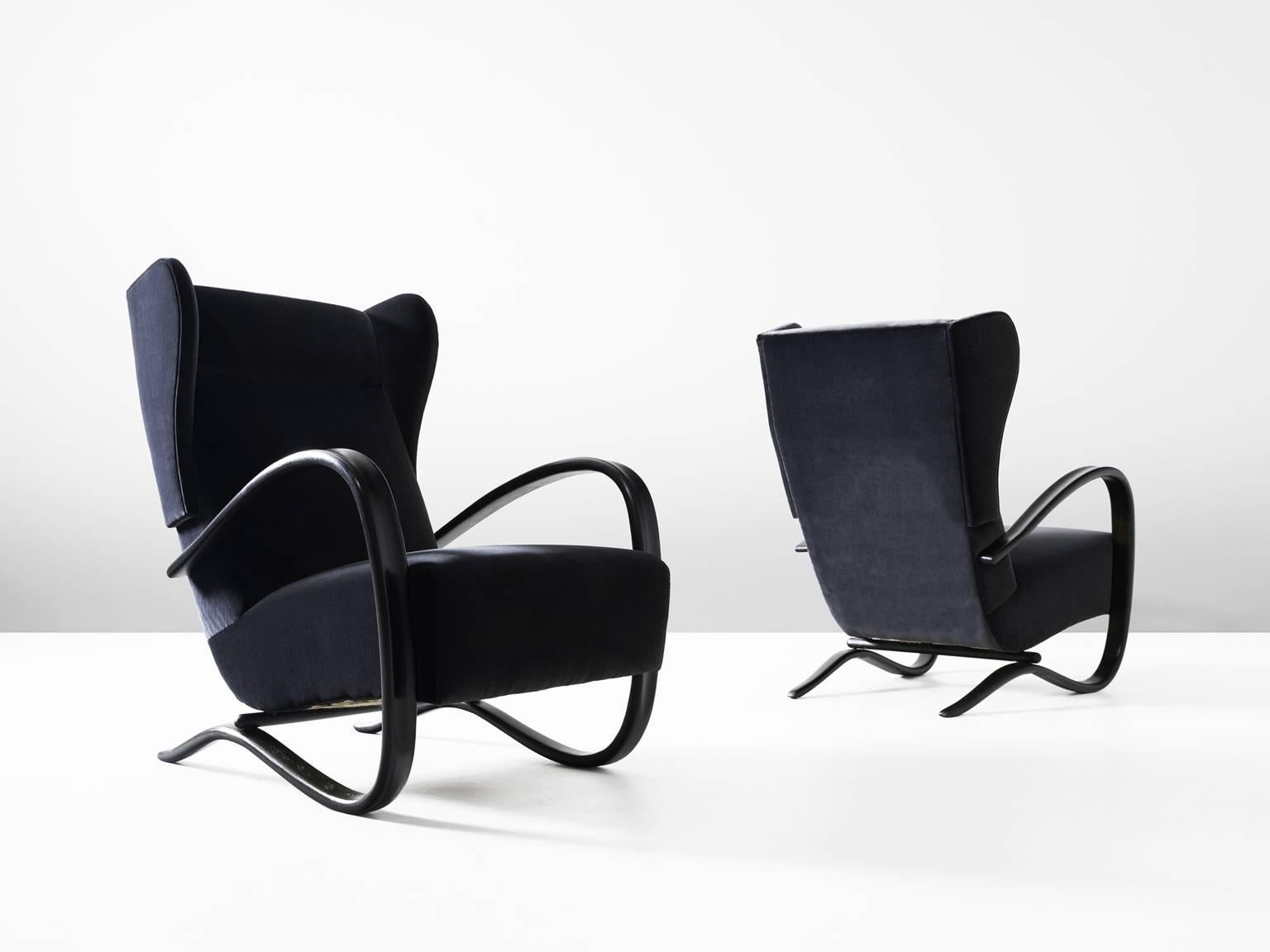 Pair of armchairs, in beech and fabric, by Jindrich Halabala, Czech Republic, 1930s. 

These lounge chairs have a very dynamic appearance, due the curved base that ends fluently in the armrests. The dark brown stained wood nicely blends with the
