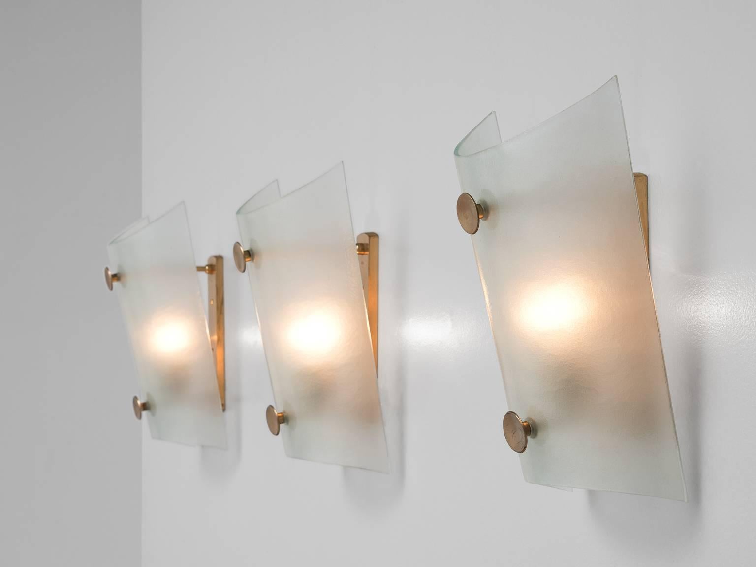 Set of three wall lights, in glass and metal, Italy, 1970s. 

Set of three interesting wall lights with a round glass shade and brass colored details. The glass has a nice structured surface with a semi-transparent look, which gives these sconces an