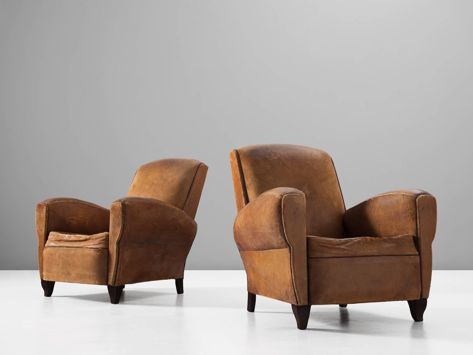 Set of two armchairs, in leather and wood, France, 1940s. 

A pair of two distressed cognac leather lounge chairs. These comfortable chairs have a stunning appearance due their patinated natural leather with beautiful worn character. Designed in Art