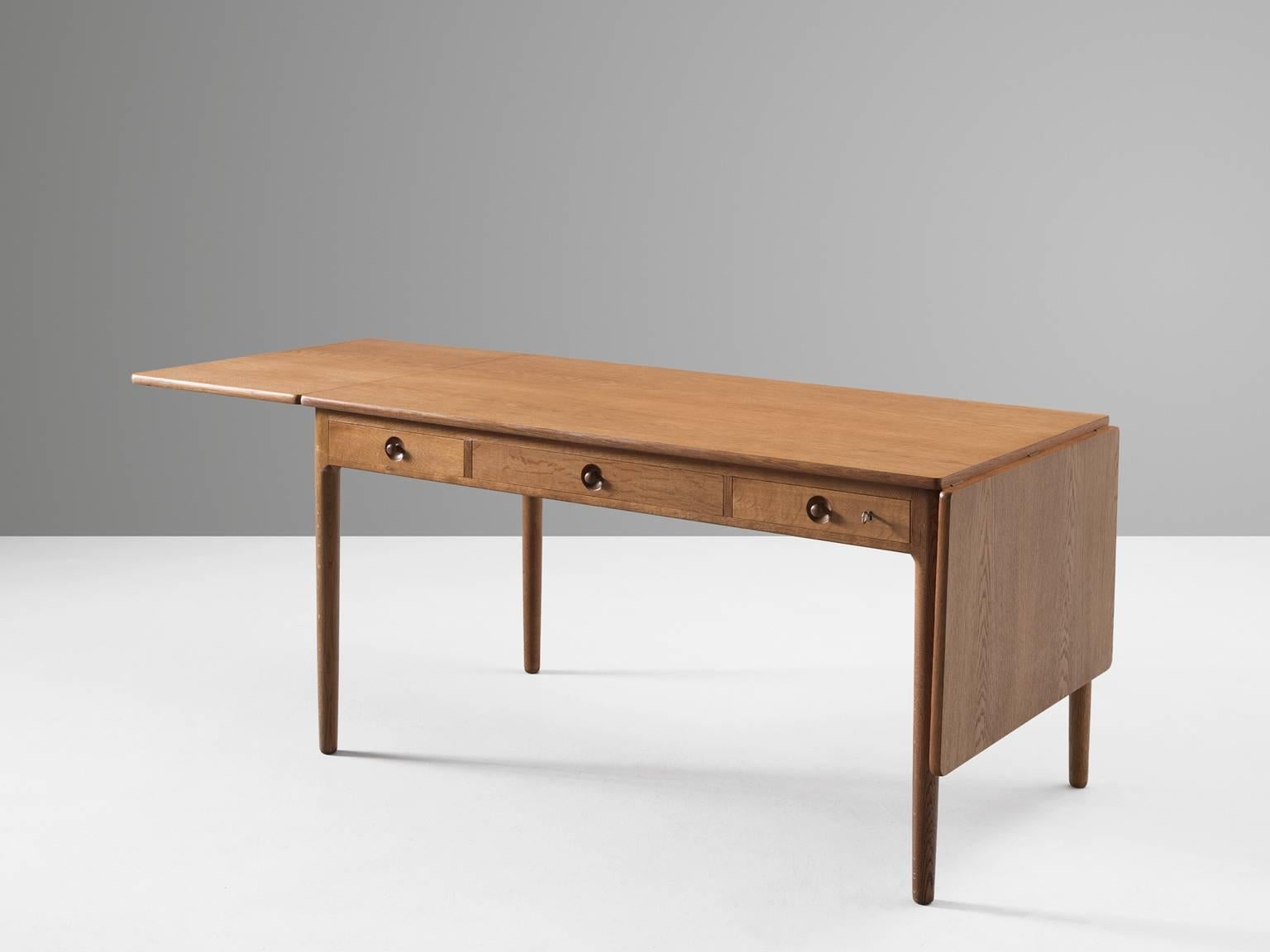 Writing table AT305, in oak, by Hans J. Wegner for Andres Tuck, Denmark, circa 1955. 

Wonderful drop leaf table by Danish designer Hans Wegner. This writing table has a drop leaf top on both sides and three drawers. Which makes it highly