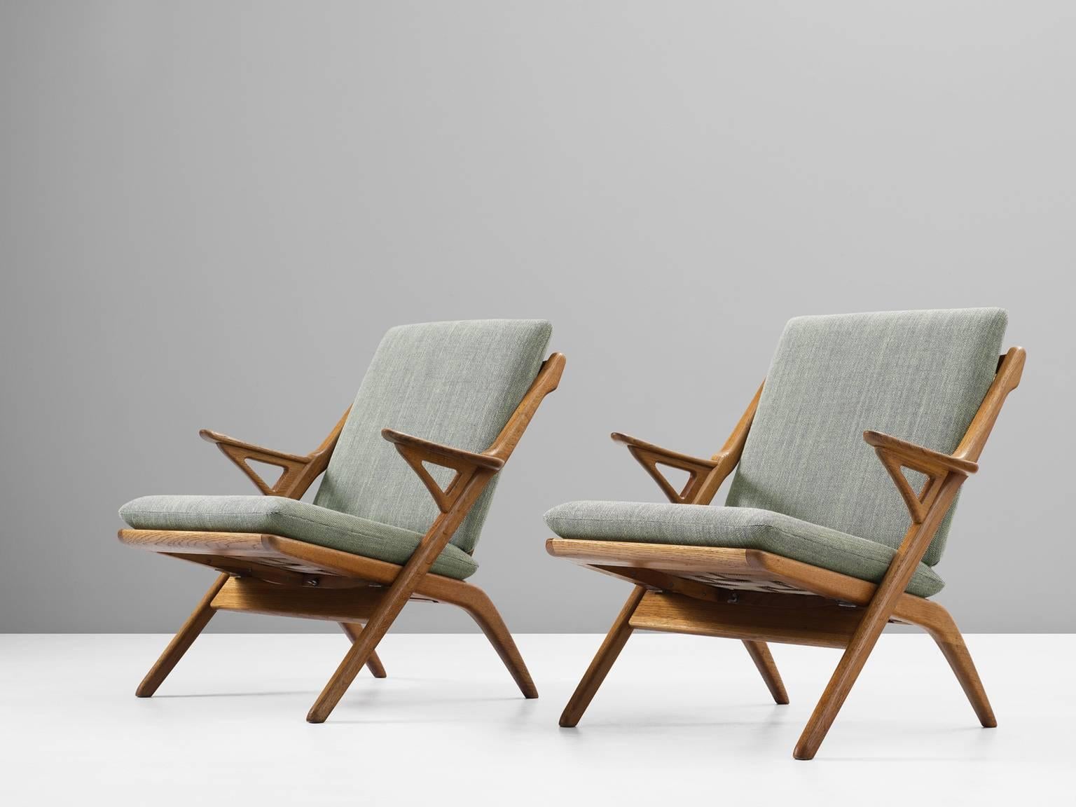 Set of armchairs, in oak and fabric, Denmark, 1960s. 

Two easy chairs in solid oak with sculptural elements. What looks like a simple folding chair is in fact a wonderful armchair, which shows a strong influence of Hans Wegner. The frame of solid
