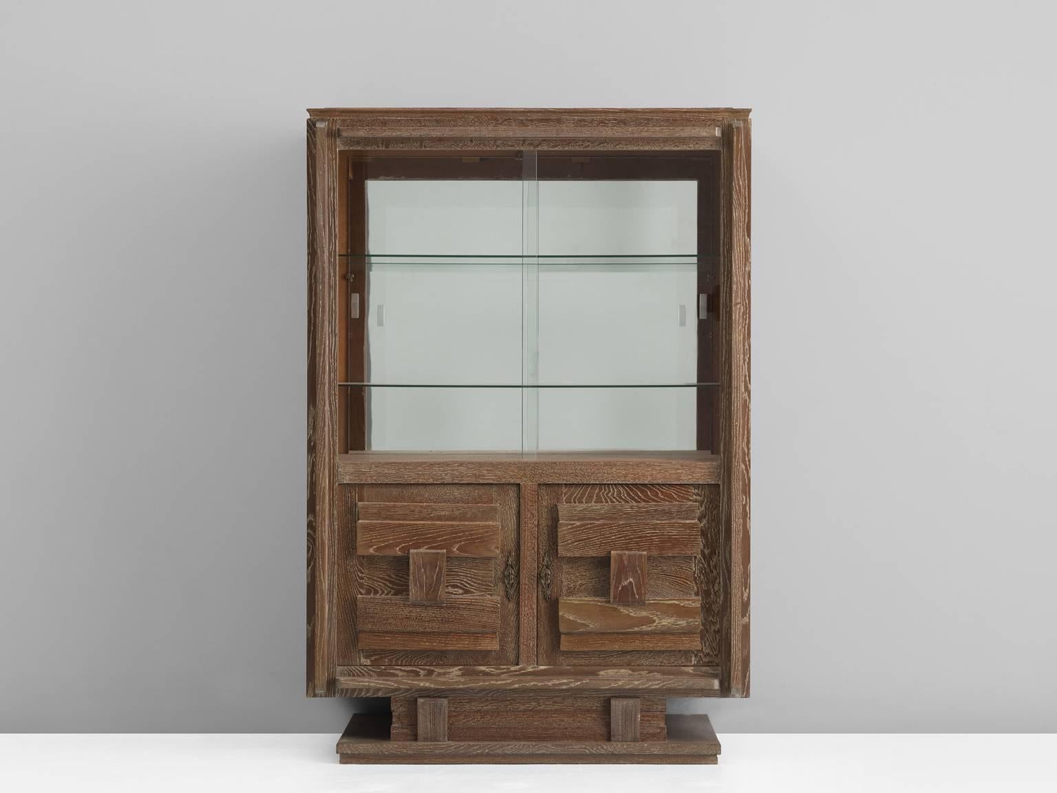 Cabinet, in glass and oak, France, 1940s. 

Nice detailed cabinet in cerused oak with glass vitrine sliding-doors. The high storage part consists of a vitrine part, with two glass shelves and a mirrored back. The lower part is a cabinet with two