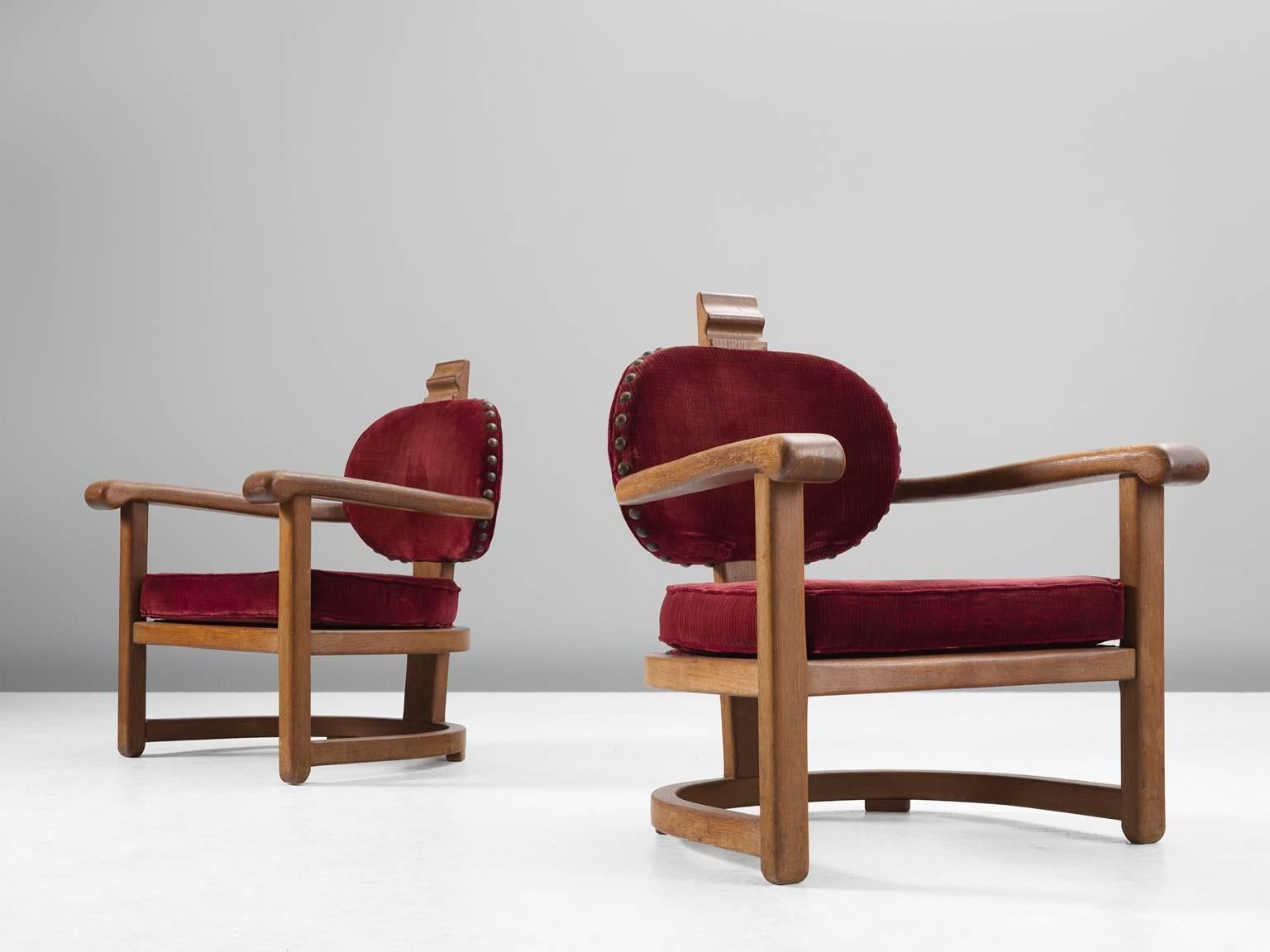 Set of two armchairs, in oak and fabric, Europe, 1930s. 

A pair of stately Art Deco club chairs with a solid oak frame and red velours fabric upholstery. These grand and solid chairs are almost architectural in the sense that they are strong enough