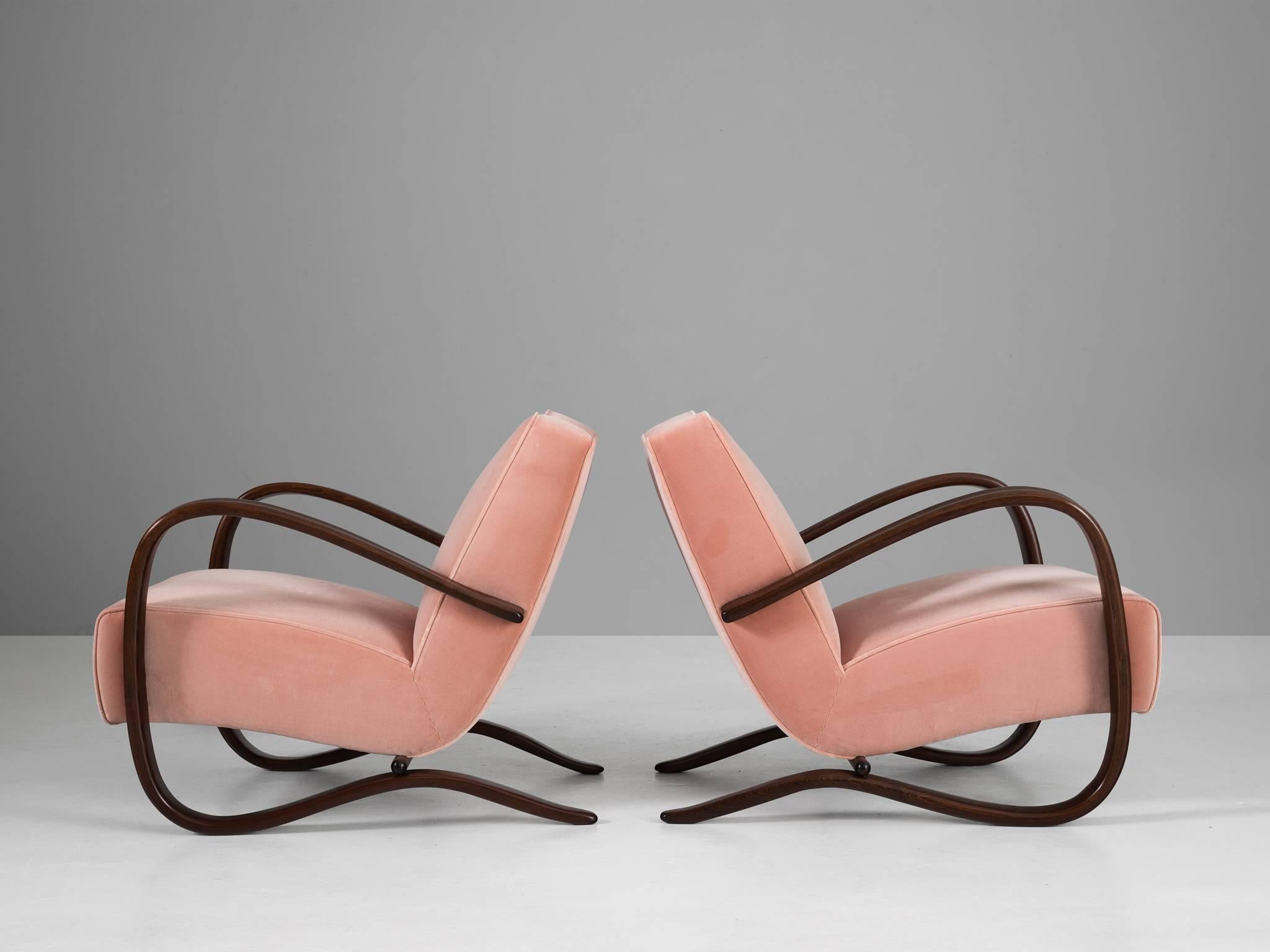 Set of two armchairs, in beech and pink fabric by Jindrich Halabala, Czech Republic, 1930s. 

These chairs have a very dynamic appearance, due the curved base that ends fluently in the armrests. The dark brown stained wood combines nicely with the