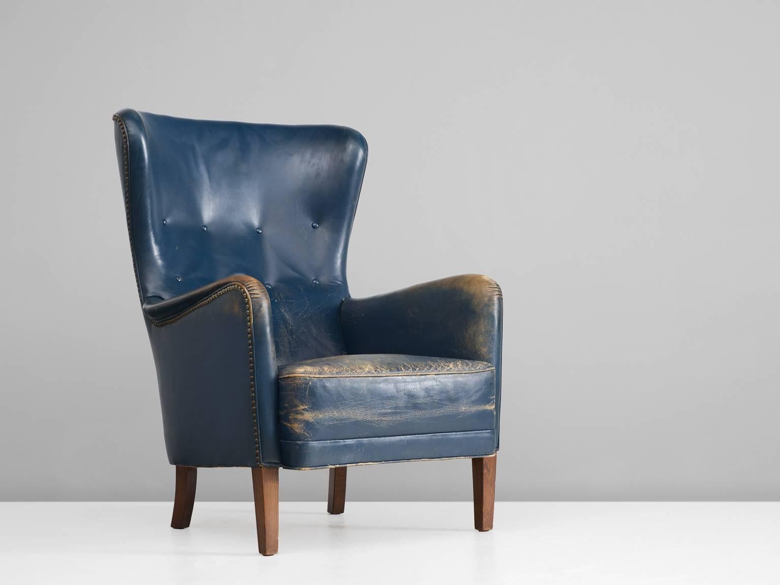 Easy chair, blue leather, brass nails, stained beech legs, Denmark, 1940s. 

This patinated wingback chair is upholstered with its original leather. The stately chair, which originates from the 1940s is the predecessor of what came to be known as