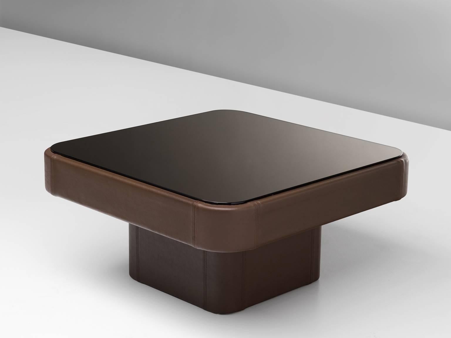 De Sede coffee table, leather, smoked glass, Switzerland, 1970s.

This robust and square cocktail table is designed by de Sede in the 1970s. The table is completely covered in dark brown leather and a smoked glass top. The black and brown are a