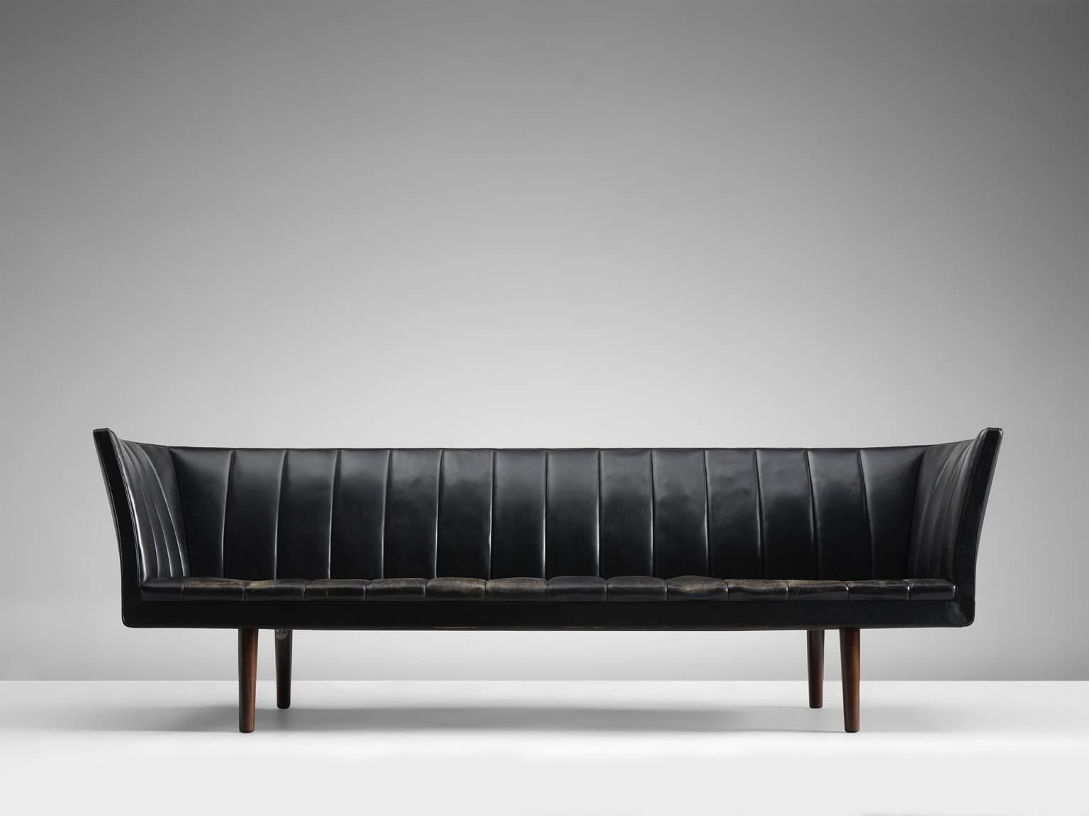 Sofa model V60, in leather and wood, by Helge Vestergaard Jensen for Peder Pederson, Denmark 1960. 

Rare three-seat sofa in black leather. High on its tapered dark wooden legs, this sofa is a beautiful sight to behold. Upholstered in black leather