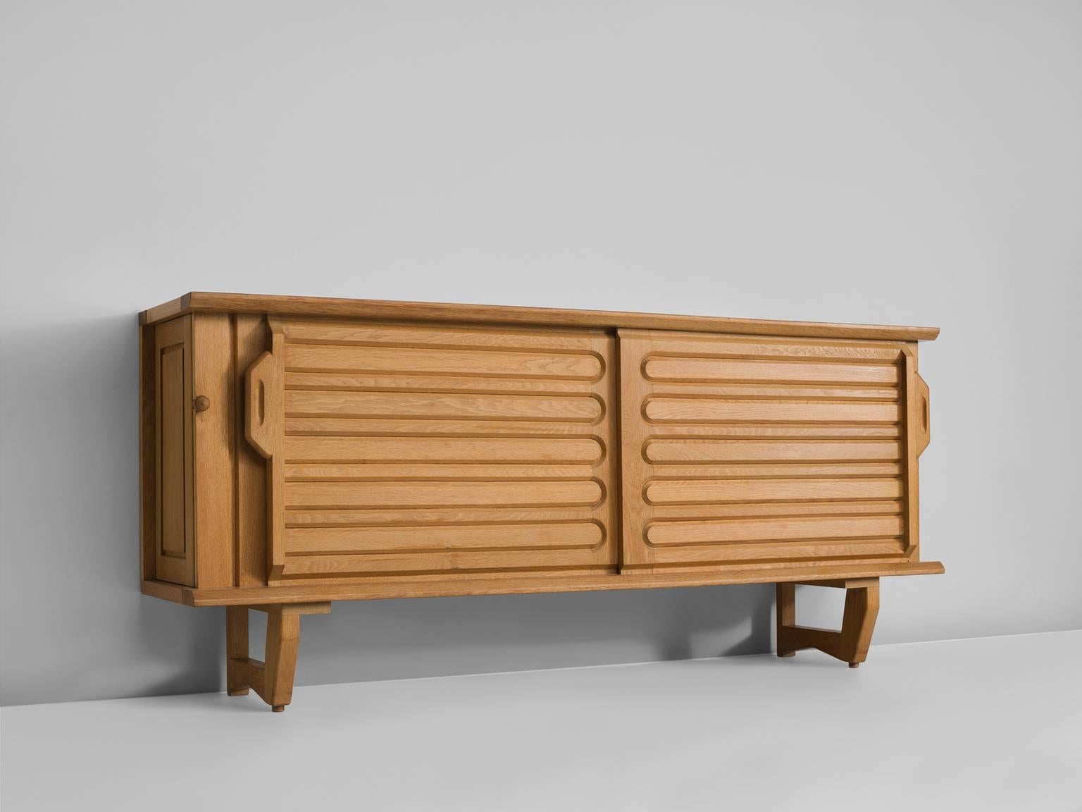 Sideboard in oak by Guillerme and Chambron, France 1960s.

Well proportioned piece, with horizontal engravings in the front sliding doors. 
The piece hides a small storage space on the side. In the top there are six colorful tiles placed into the