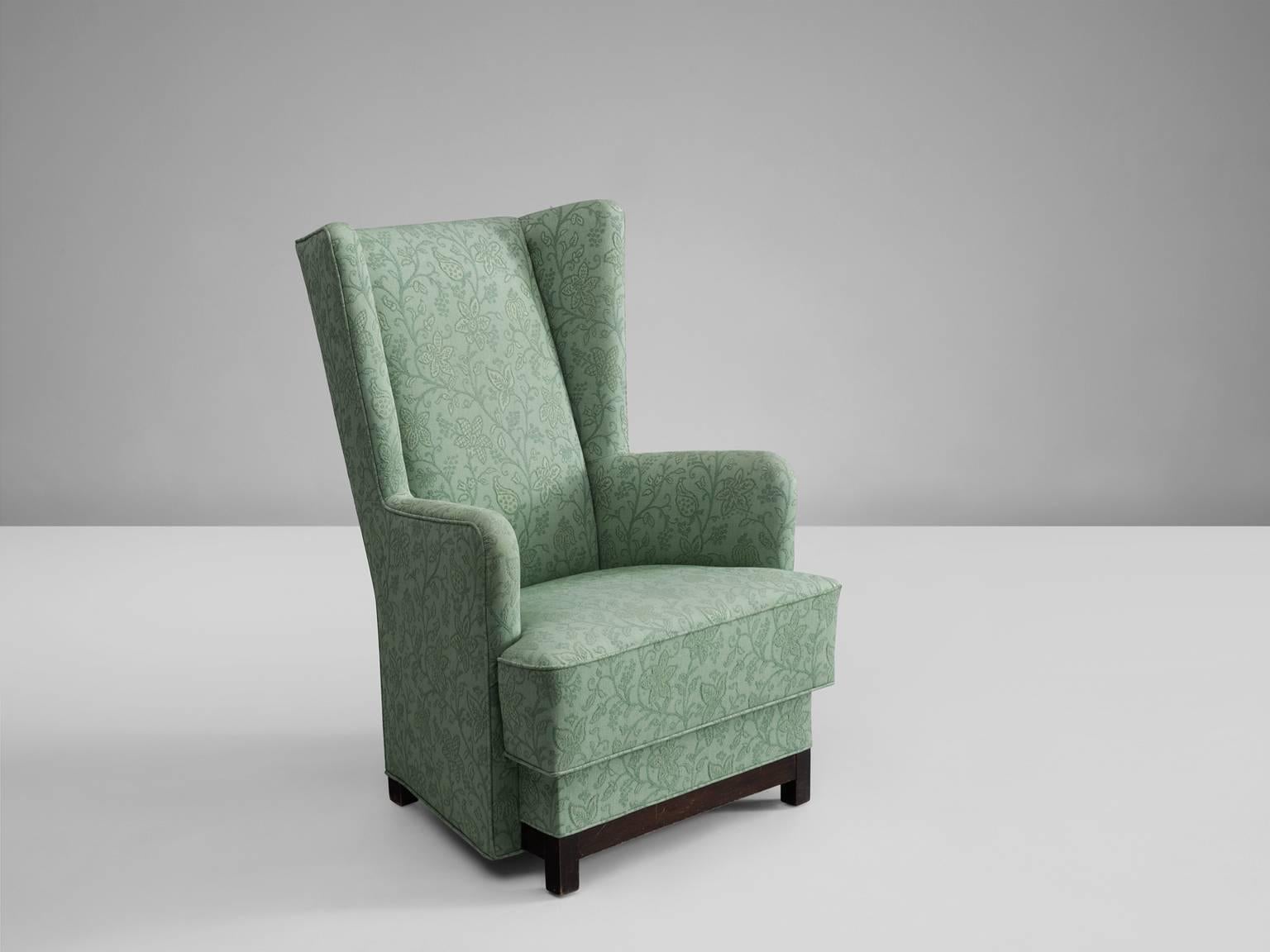 Danish armchair in original green floral upholstery, 1940s.

This comfortable high wing back chair has straight lines and a basic wooden frame.
Reupholstery is possible if required. 

The highly experienced craftsmen of our in-house atelier are