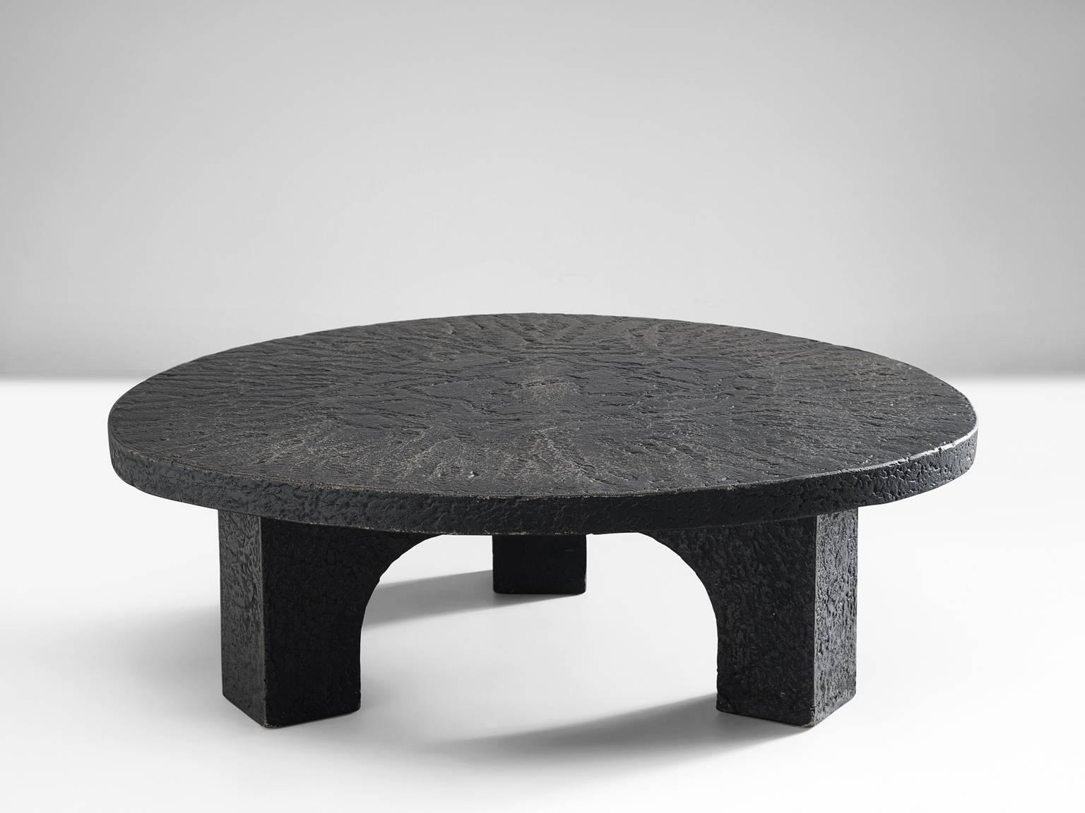 Round cocktail table, resin, Northern-Europe, 1970s. 

This architectural black coffee table is from the 1970s. The round top is supported by an architectural base. This low table is made out of resin yet resembles the appearance of stone.