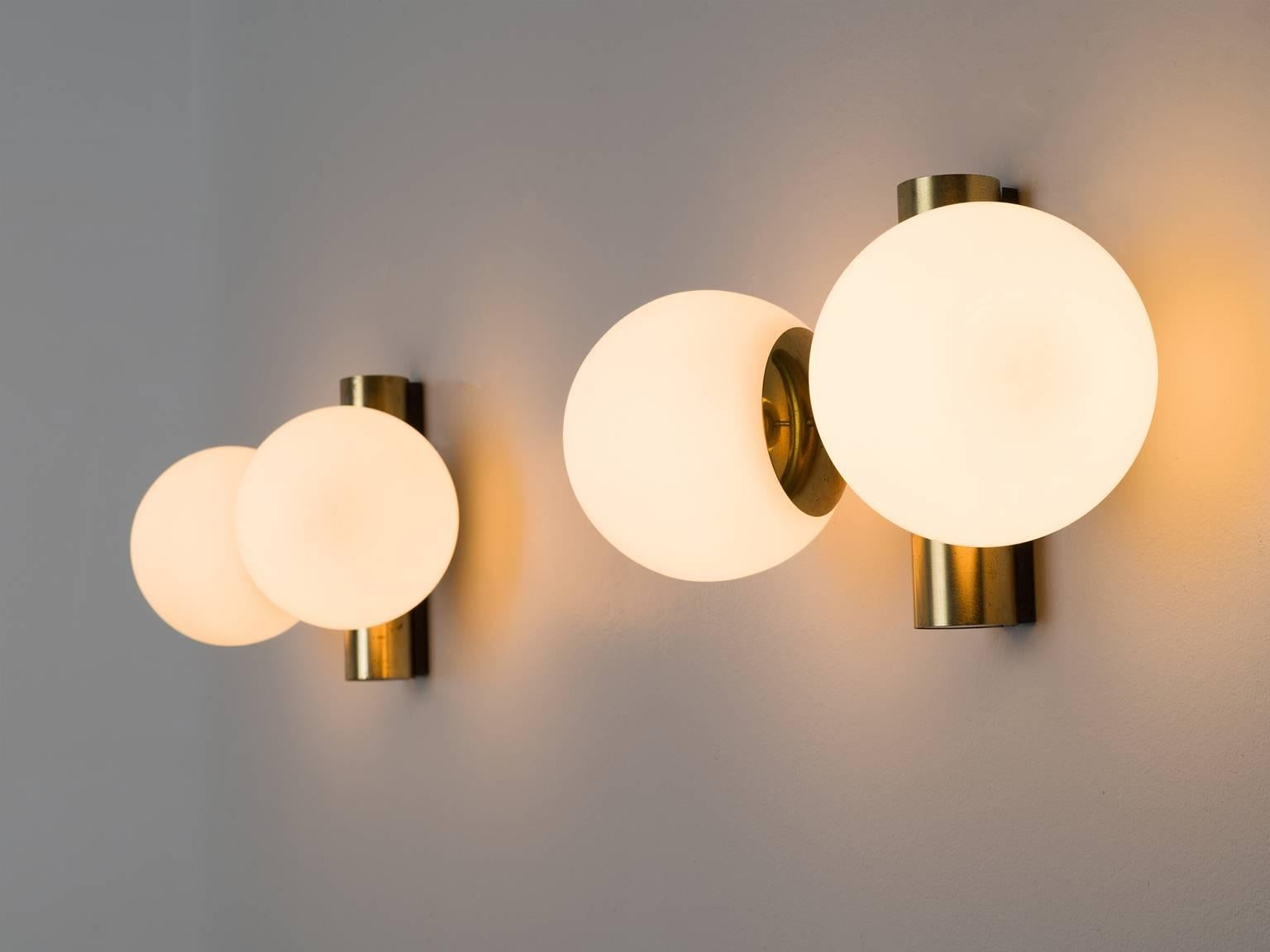 Wall lights in brass and opaline glass, Europe, 1960s. 

Set of two solid brass sconces with glass shades with a warm opaline white shade. The lights each have two short arms ending in a glass light bulb. These wall scones have a very natural light