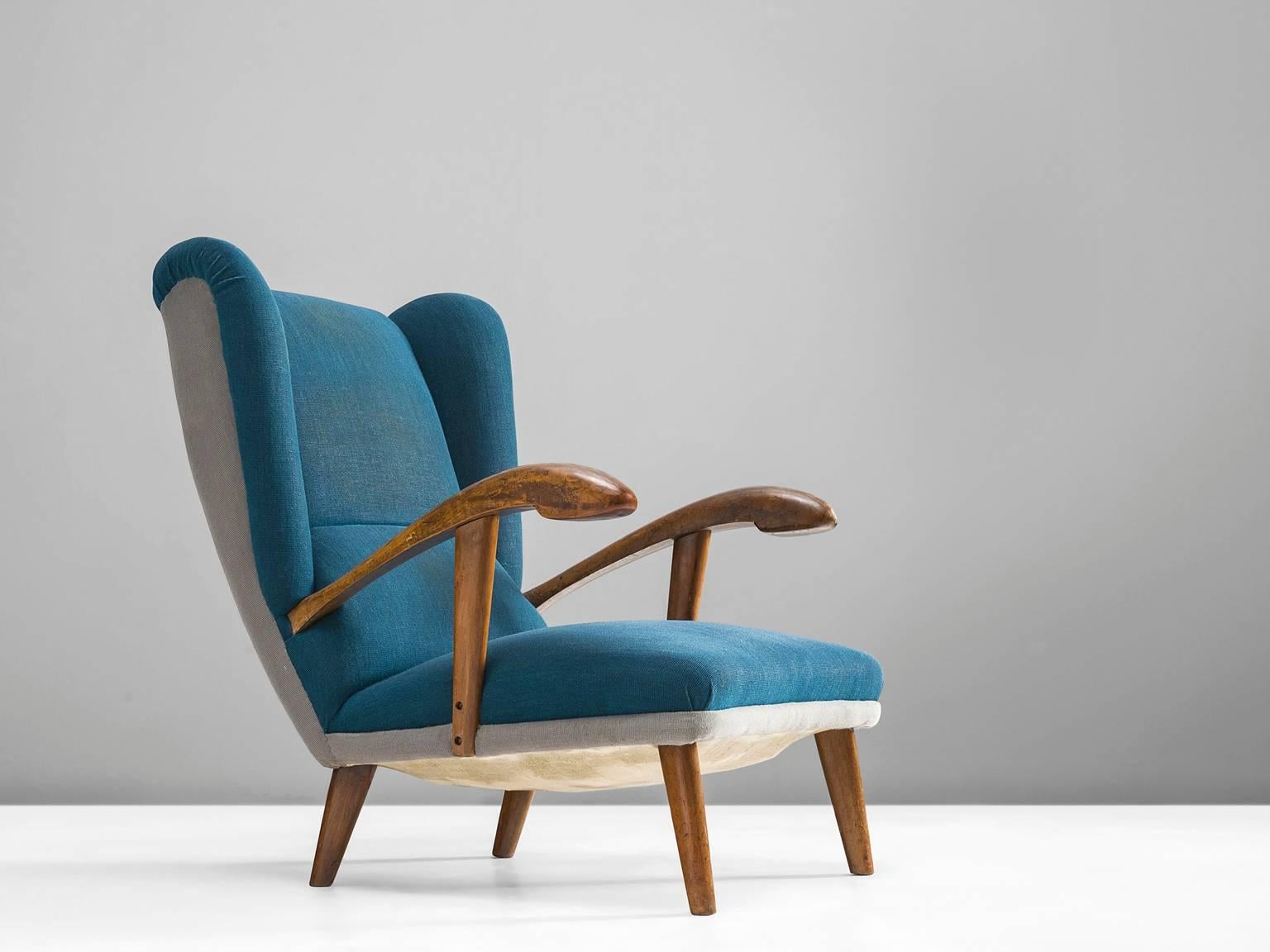 Easy chair, wood, blue and white fabric, Europe, 1940s

This strong, playful wingback chair is designed with a slightly tilted back in order to provide sitting comfort. The wooden armrests are pointing upwards and flow gracefully from the backrest