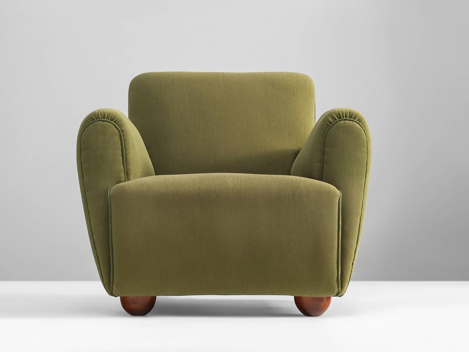 Lounge chair, green fabric, wood, Europe, 1950s.

This Mid-Century armchair is densely designed, featuring thick armrests seat and backrest with no open space or detailing apart from the piping on the front of the armrests. The feet are
