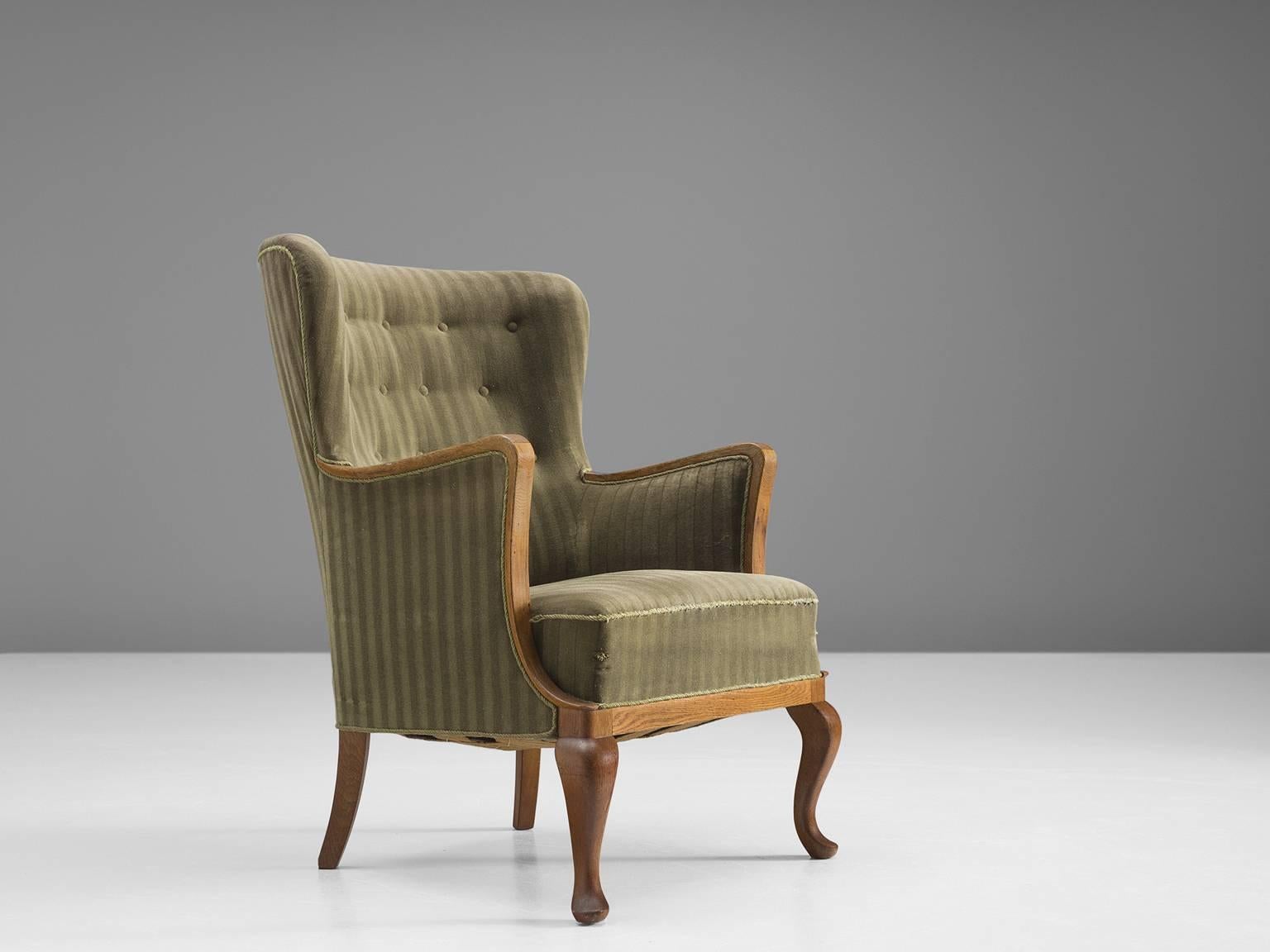 Armchair, green and wood, Denmark, 1950s.

This stately and comfortable wingback chair holds the middle between Classic wingback chairs and Scandinavian Modern design. The legs and armrests are executed in wood whereas the rest of the chair is