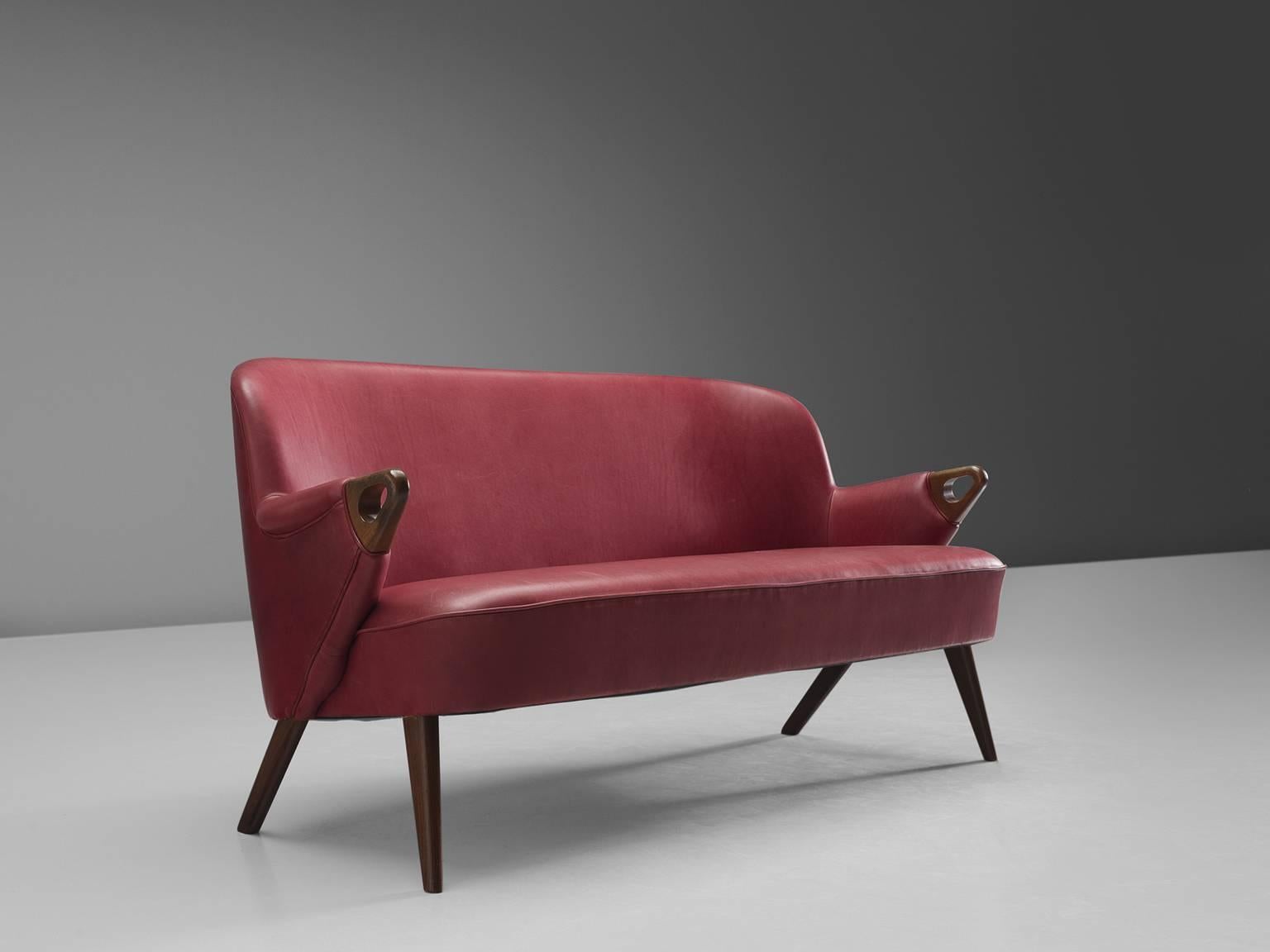 Two-seater sofa, leather and teak, 1960s, Denmark.

This small sofa features a simplistic, red leather shell and well-worked out detailing in the armrests and legs. The ends of the armrests are detailed with rounded triangles that are the end