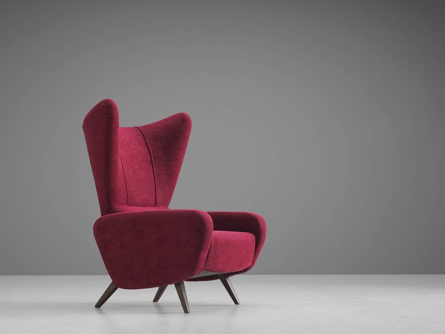 Large Italian wingback armchair in the style of Gio Ponti, red to pink fabric, ebonized conical wood legs, Italy, 1950s.

This Classic Italian wingback chair has all the traits of Midcentury Italian design. The unusually high back, the gracious