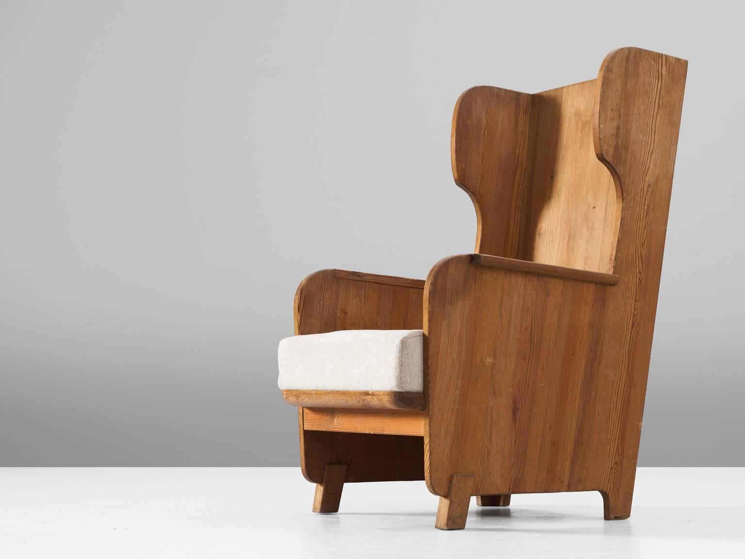 Axel Einar Hjorth for Nordiska Kompaniet, wingback chair 'Lovo', in pine and fabric, by Sweden, 1932. 

Sturdy high back chair in solid pine by Axel Einar Hjorth. This chair has all classical elements of a wingback chair, yet due the execution in