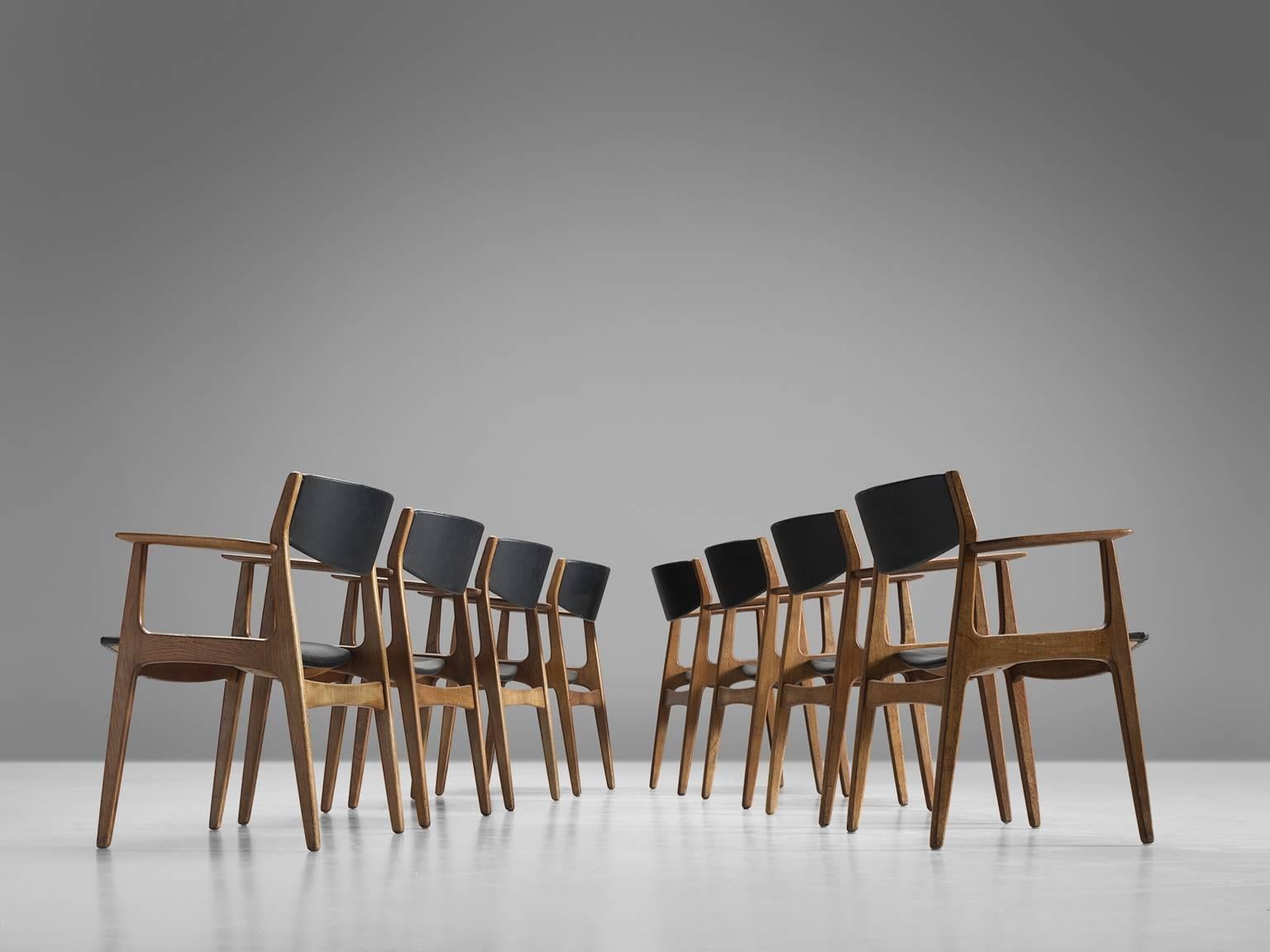 Henning Kjærnulf for Sorø Stolefabrik, set of eight armchairs, oak, black faux leather, Denmark, designed 1960. 

This set of solid, stately dining chairs is executed in solid oak and black leatherette. The set is sculptural and well-executed.