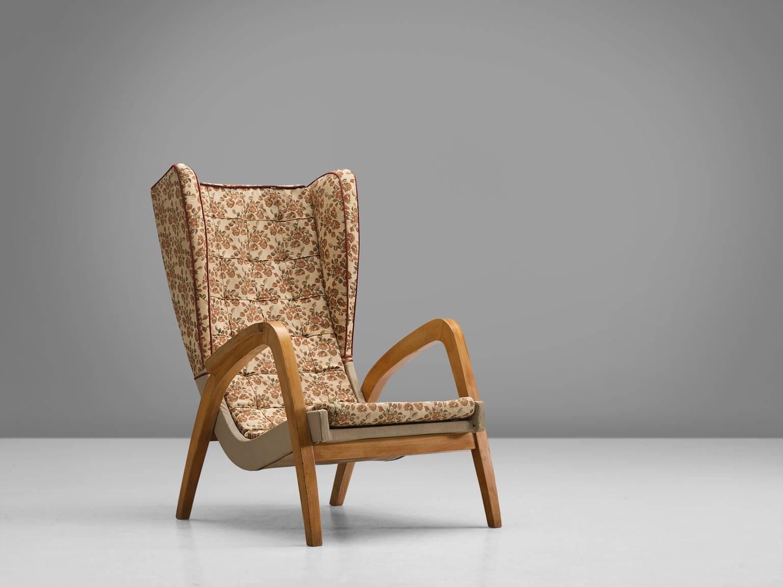 Easy chair, wood, beige floral fabric, United Kingdom, 1940s

This strong, playful wingback chair is designed with a slightly tilted back in order to provide sitting comfort. The wooden armrests are pointing upwards and flow gracefully from the