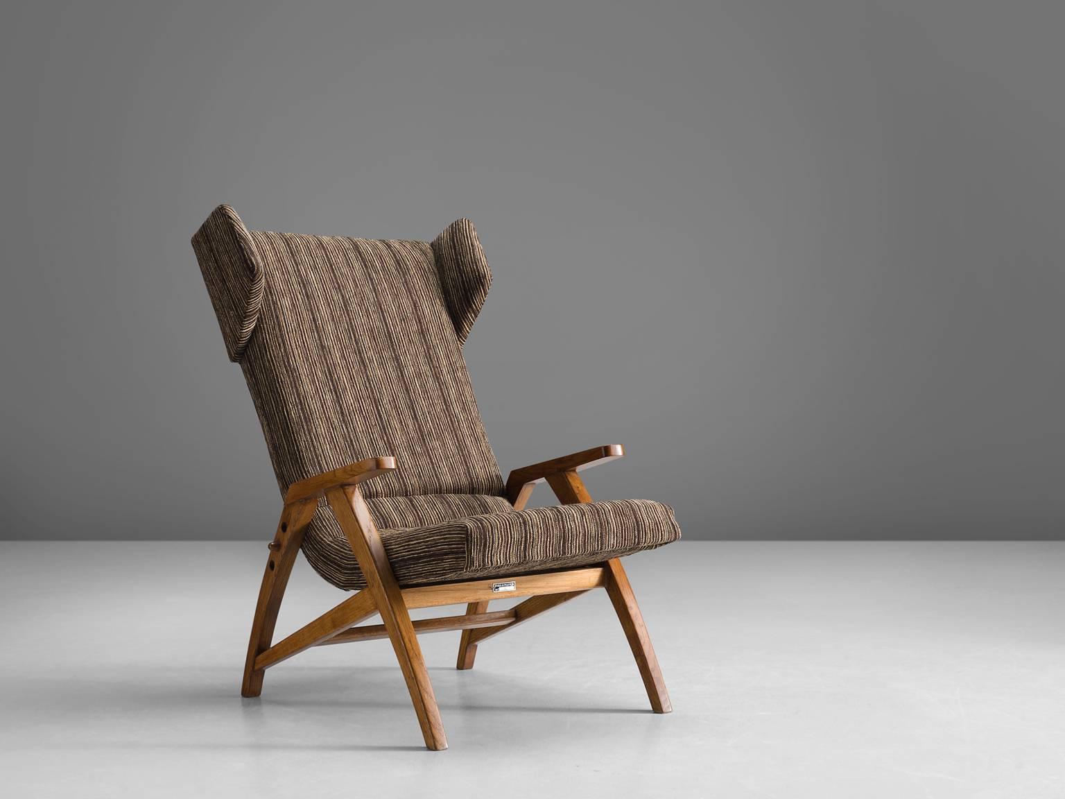 Easy chair, wood, beige brown fabric, oak, Czech Republic, 1940s.

This strong, playful wingback chair is designed with a slightly tilted back in order to provide sitting comfort. The wooden armrests are pointing upwards and flow gracefully from the