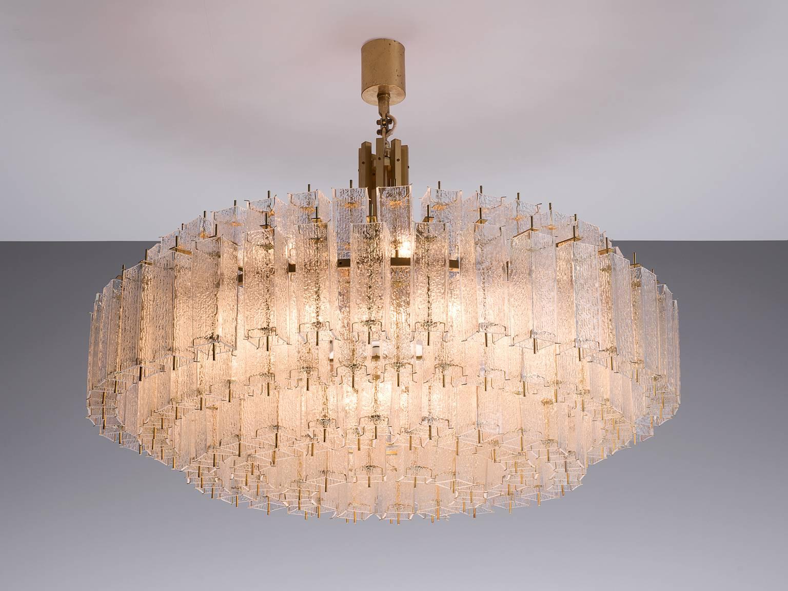Chandelier, in glass and brass, Europe, 1970s. 

Large circular 160cm/5ft chandelier with three layers of glass shades. The frame is made of brass and holds numerous structured glass 'tubes' with a brass centre. Due the combination of materials