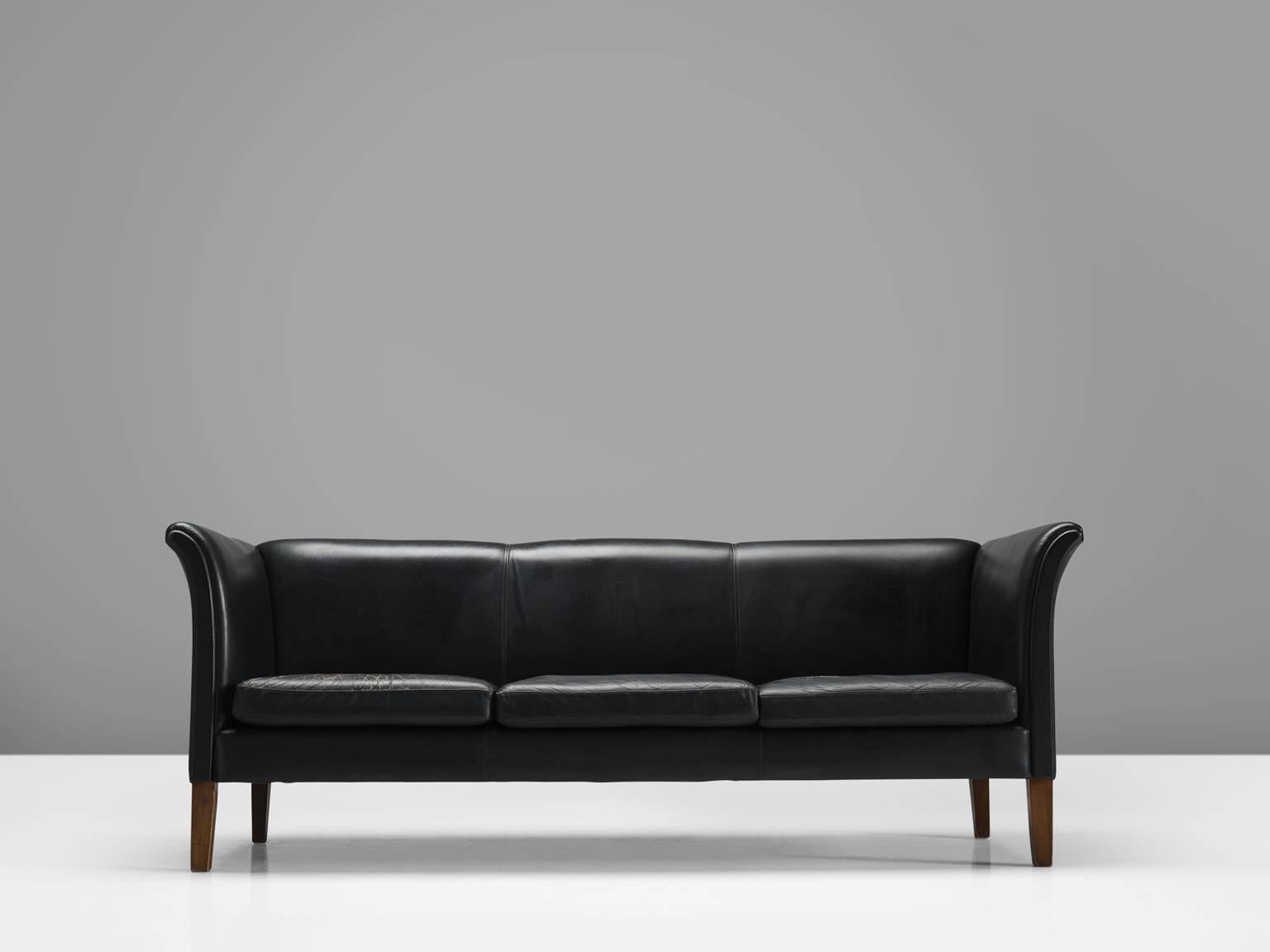 Sofa in leather and wood, Sweden, 1960s. 

Three-seat sofa in high-quality black faux leather. The wooden legs provide a floating appearance to this comfortable sofa. The armrests are beautifully curved and give this sofa it's strong expression by
