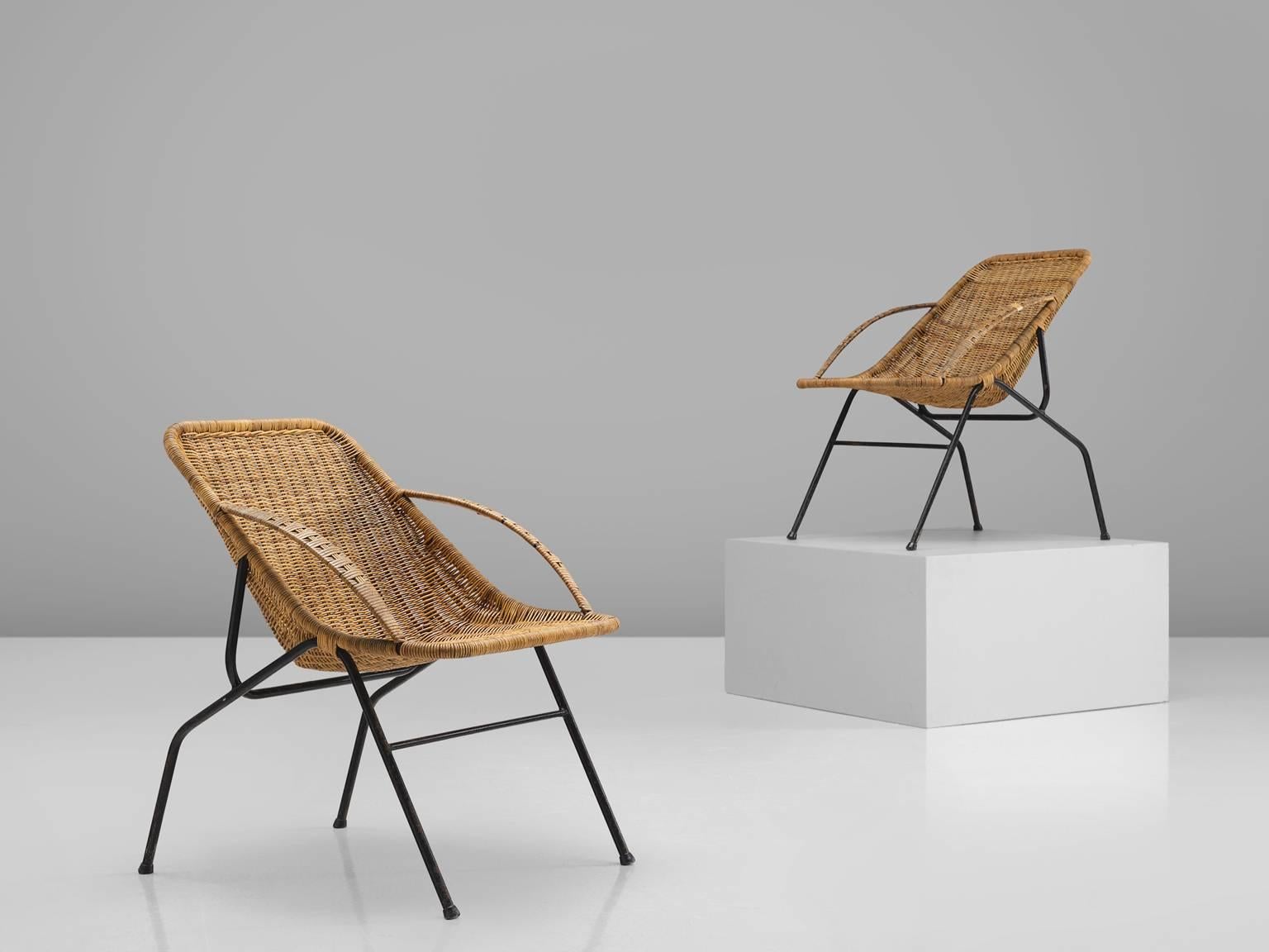 Armchairs, rattan, cane and black coated metal, France, 1950s.

This pair of cane chairs are executed with a rattan shell with two woven cane armrests. The seat is slightly tilted. The frame is black and sculptural and the chairs show strong