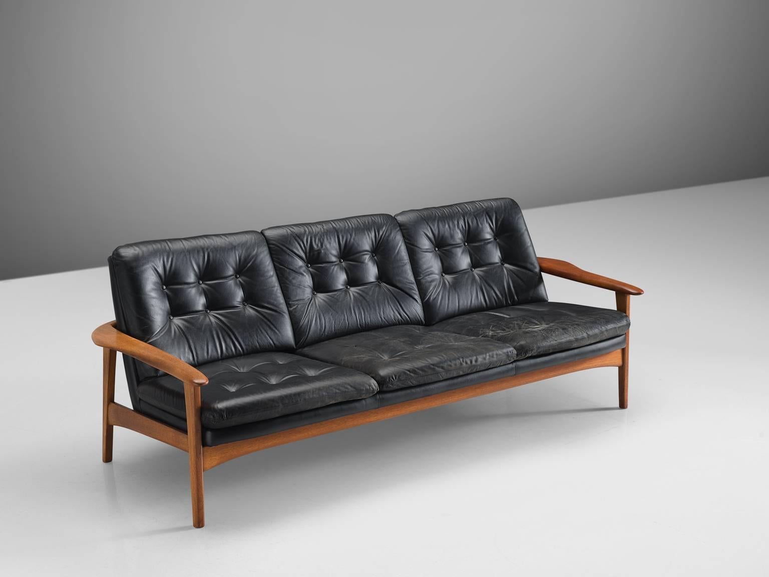 Settee, black leather and teak, Denmark, 1960s.

This three-seat sofa features a teak frame and the back and seat are upholstered in a black tufted leather. The armrest are curved and flow slightly inwards. The sofa's prime distinction is its