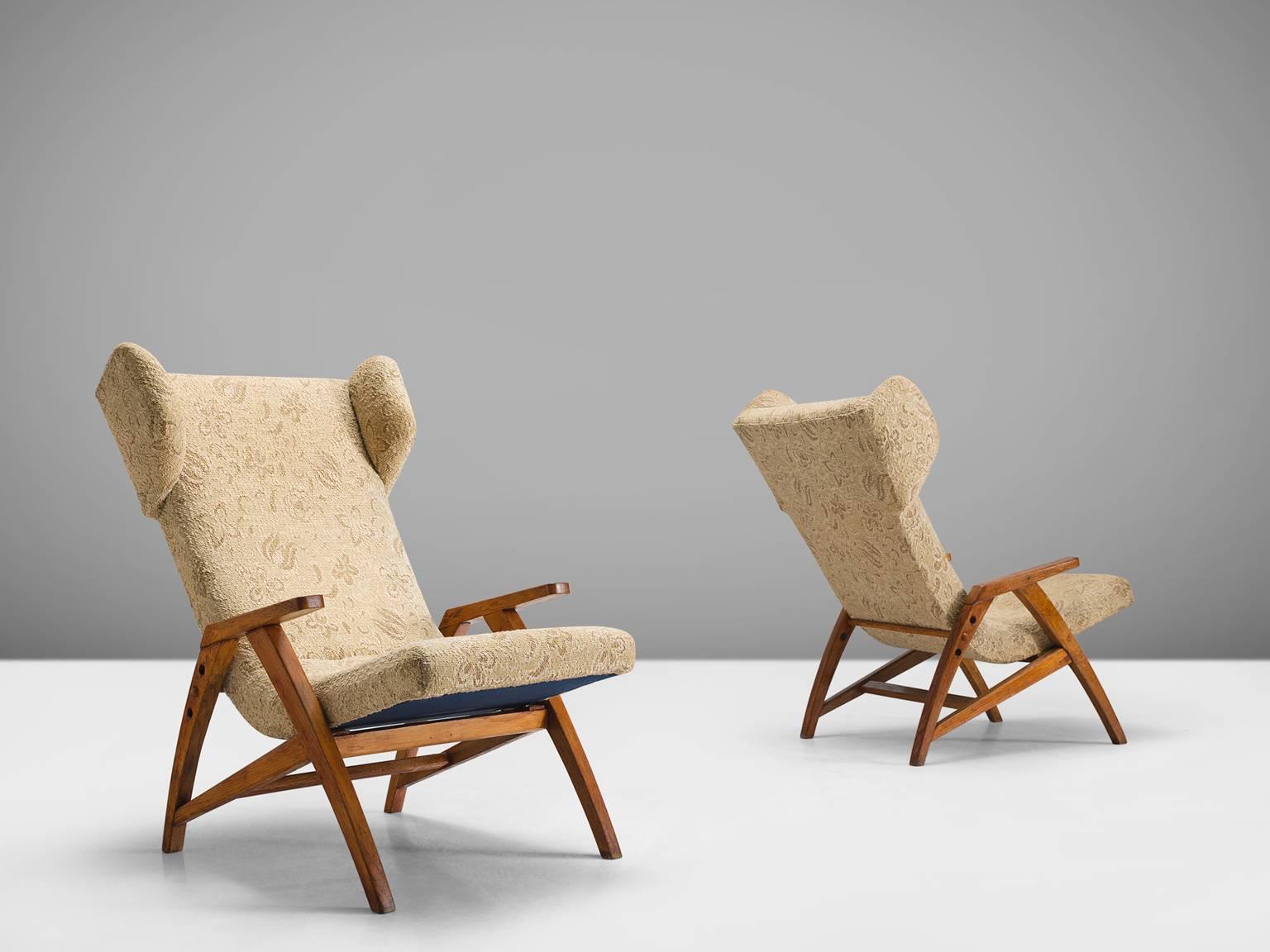 Easy chairs, wood, beige brown fabric, oak, Czech Republic, 1940s.

Two strong oak wingback chairs designed with a slightly sloped back in order to provide sitting comfort. The chair features small, geometric wings that are separated from the the