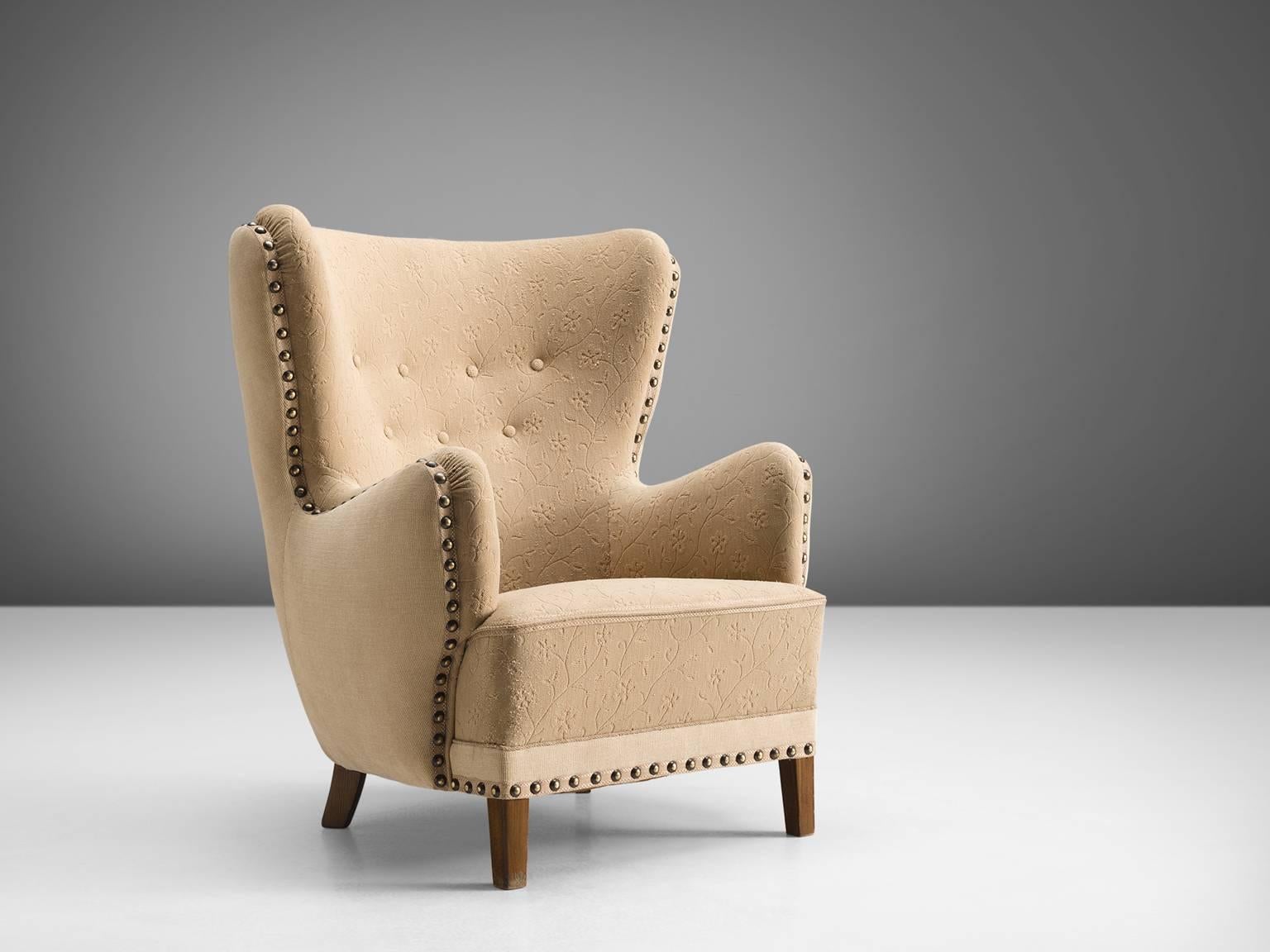 Danish cabinetmaker, lounge chair with stained beech legs and beige fabric, Denmark, 1950s 

This easy chair with stained beech legs features a modest wing and buttoned back. The seat is thick and the armrests are rounded. The frame of the chair is
