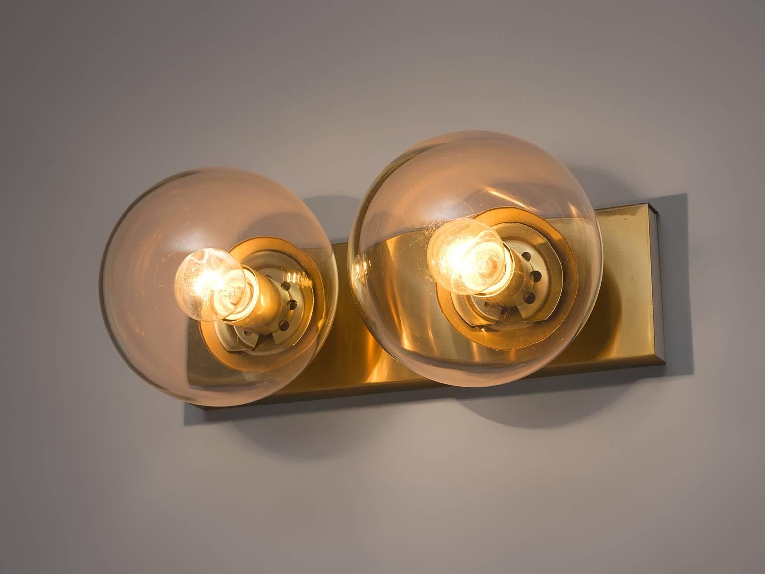Wall lights in brass and opaline glass, Europe, 1960s. 

Set of four double wall sconces with clear glass shade. The bulbs are connected directly to a brass horizontal slat that is connected directly to the wall. These wall scones have a very